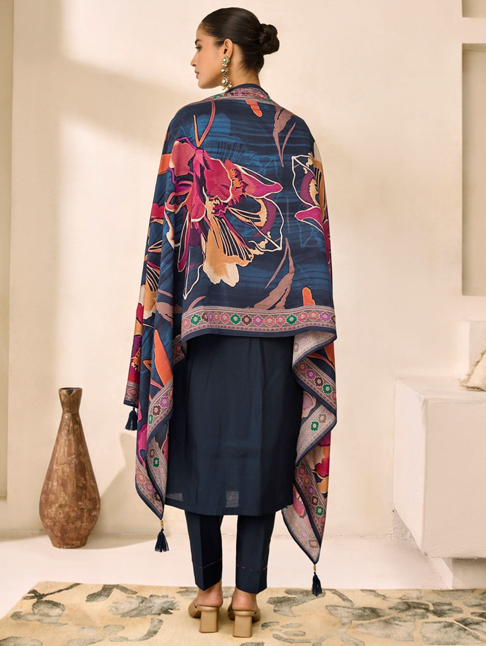 Woman wearing a colorful floral patterned shawl over a dark outfit in a minimal indoor setting.