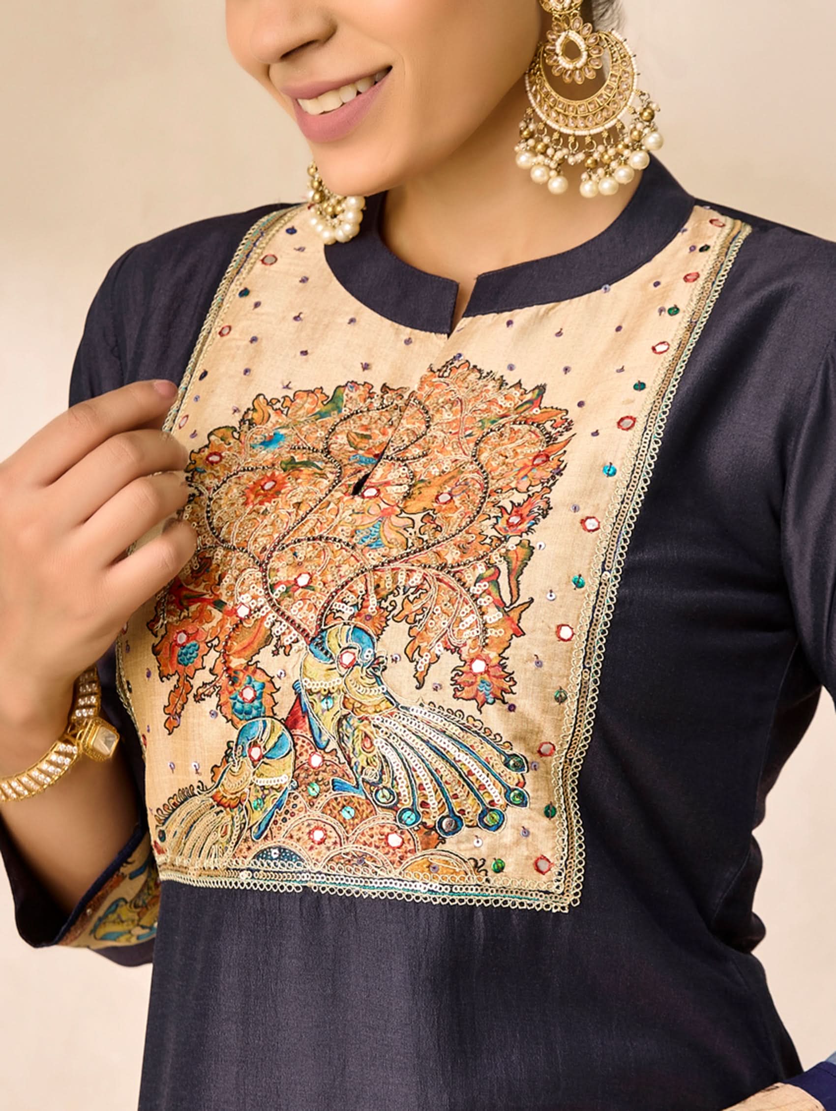 Woman wearing a navy blue outfit with a decorative beige blouse featuring intricate designs.