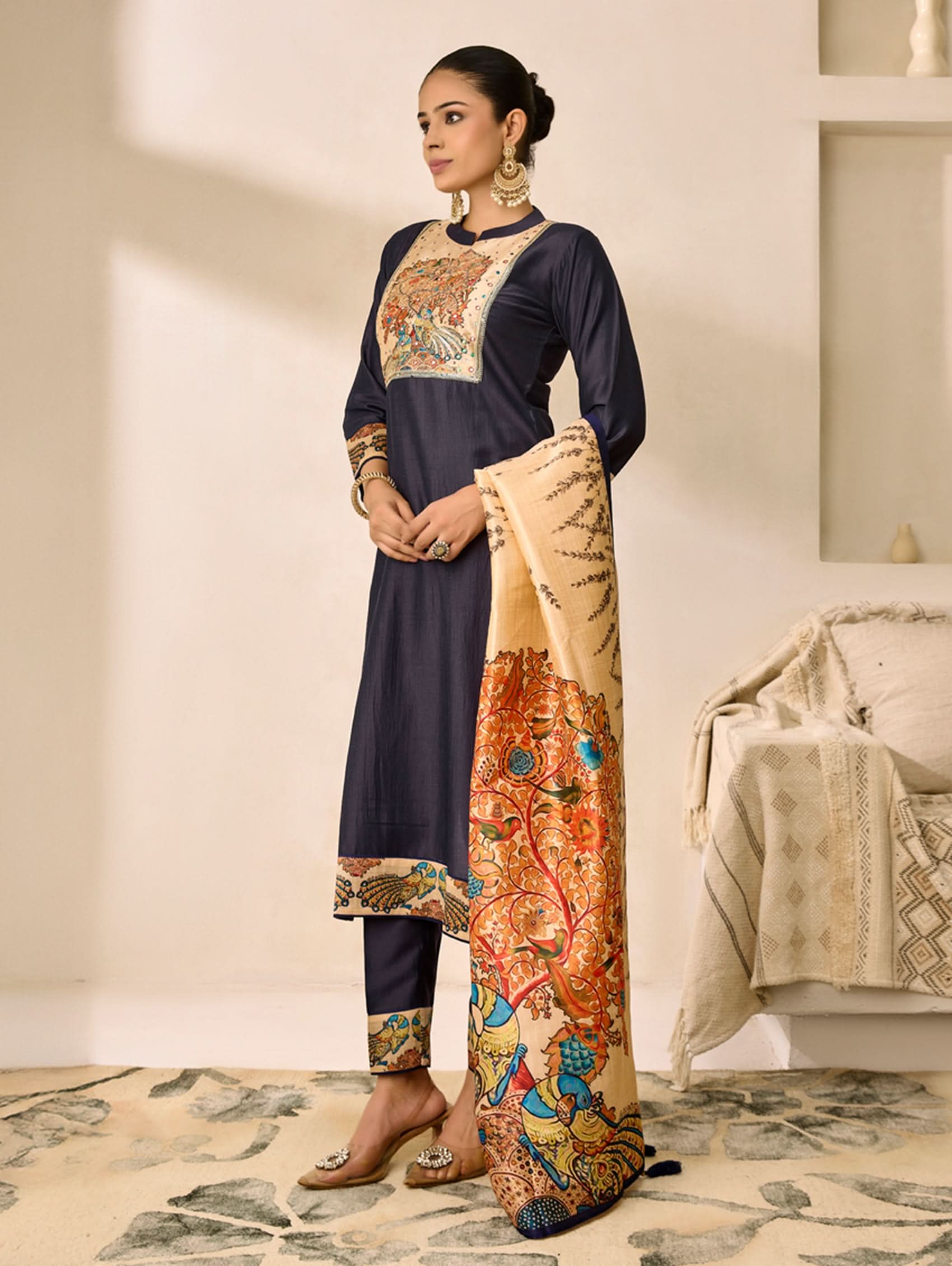 Woman wearing a traditional outfit with intricate patterns in a minimalistic room.
