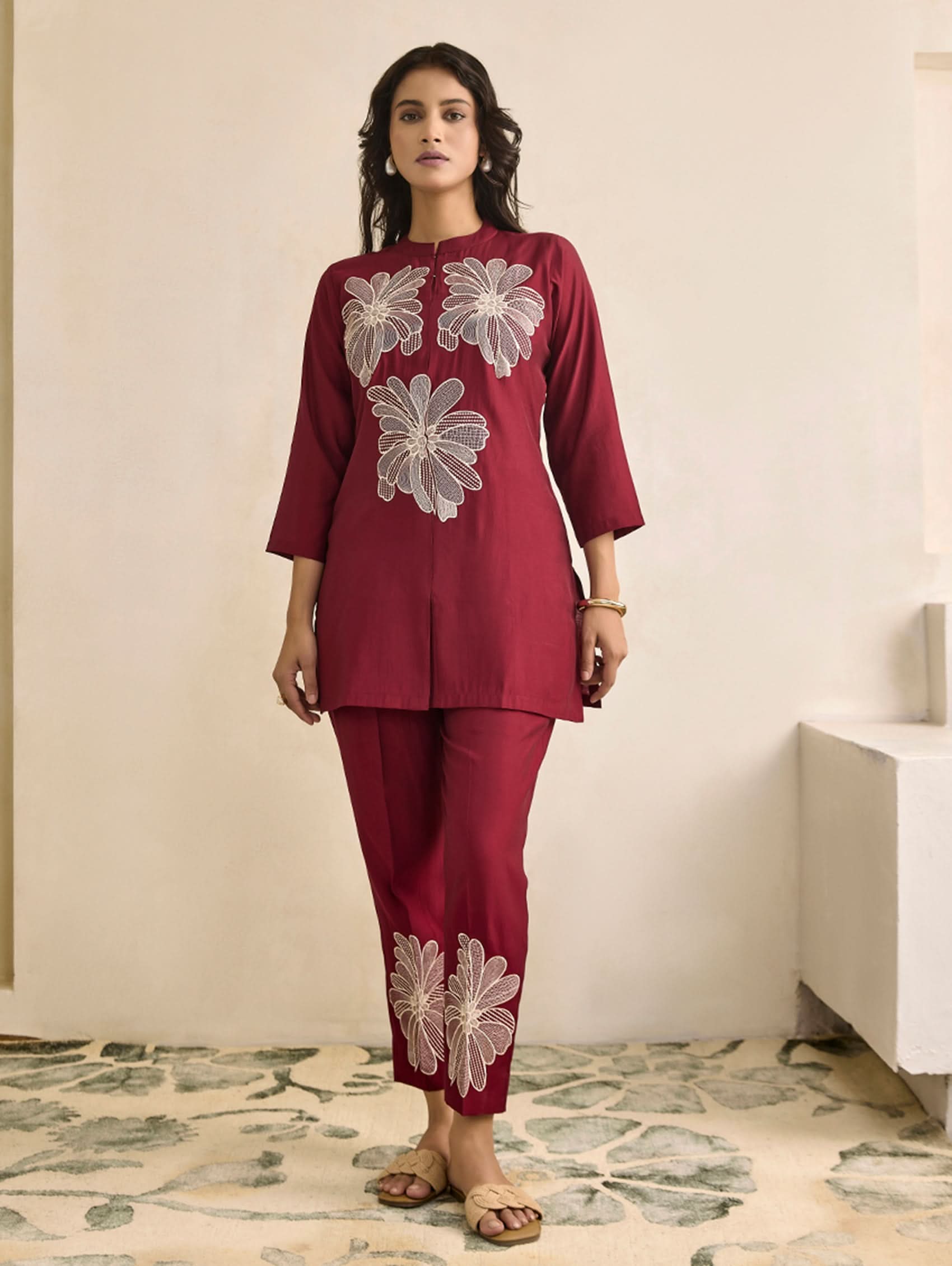Woman wearing a maroon outfit with floral embroidery in a room with a floral rug.