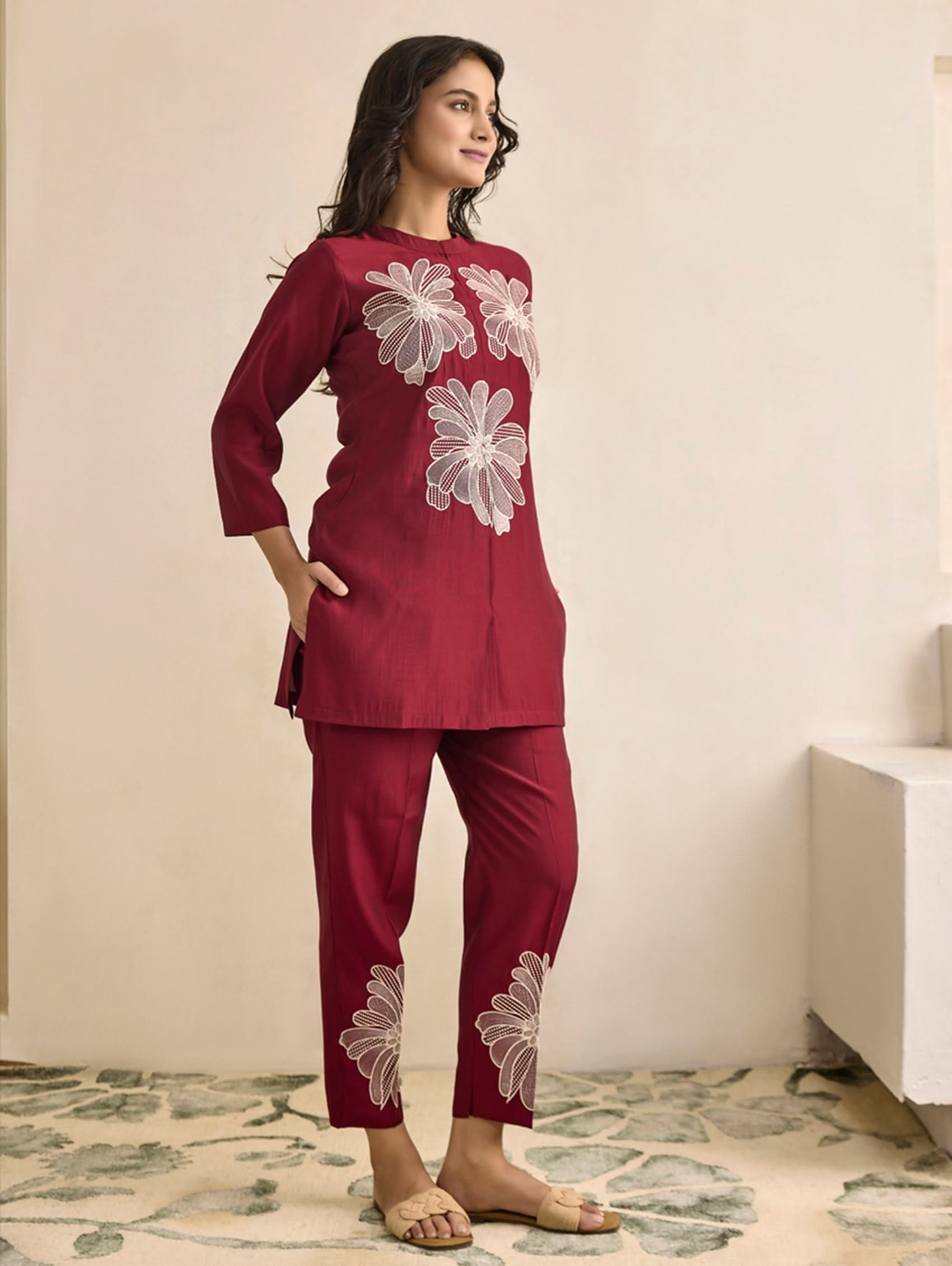 Woman wearing a maroon outfit with floral embroidery in a minimal indoor setting