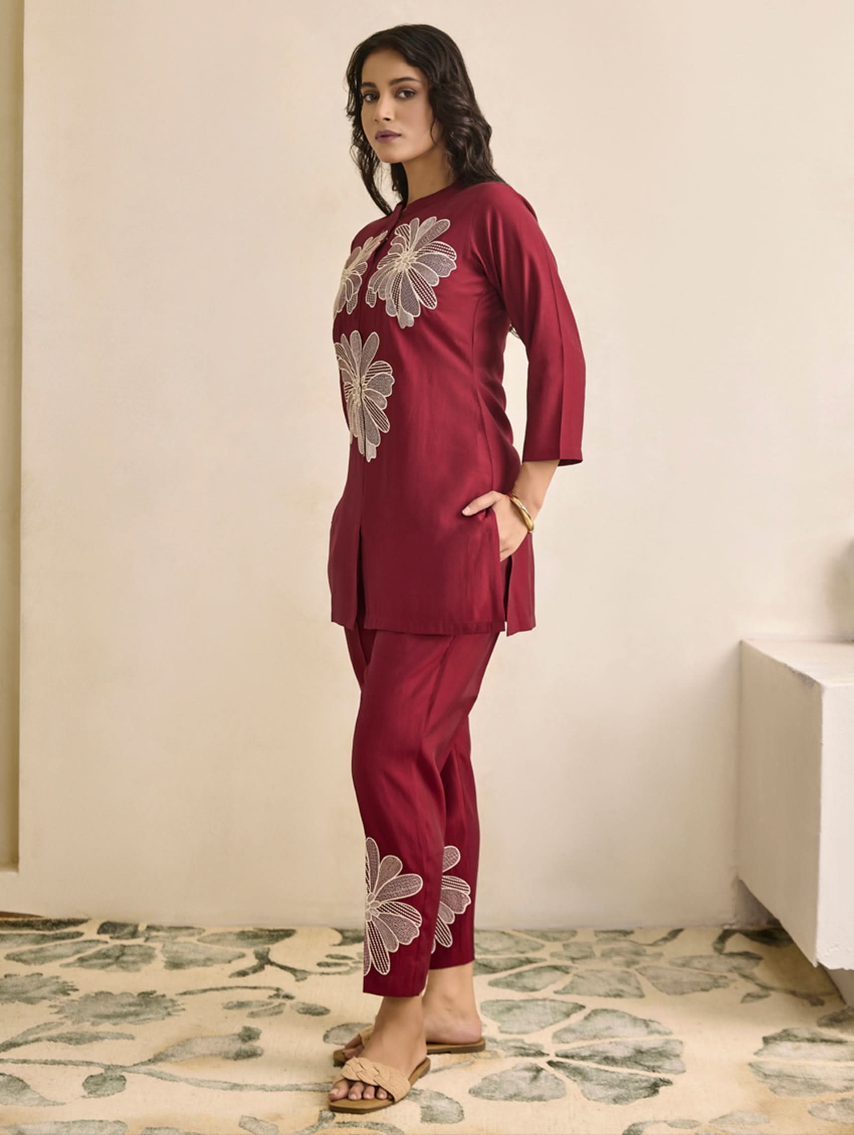 Woman wearing a maroon outfit with floral embroidery in a room with a stone floor.