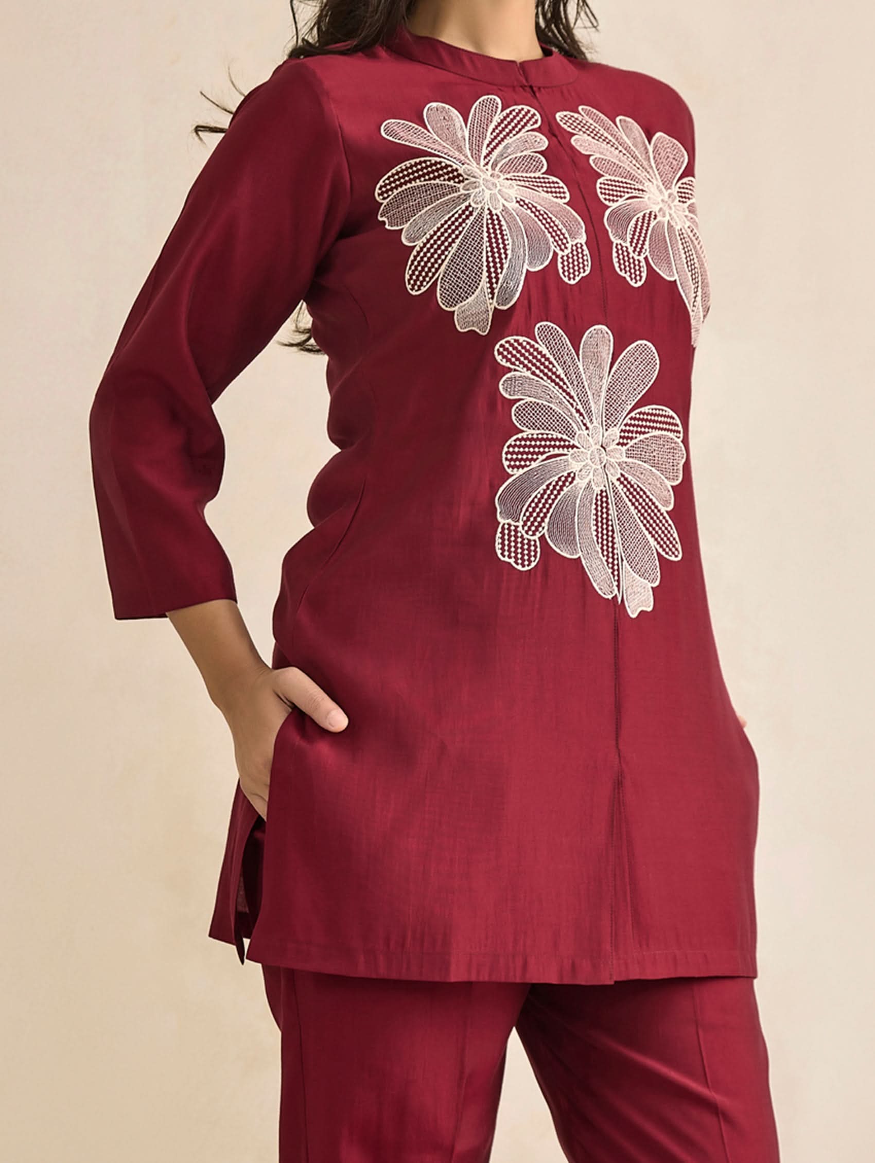 Maroon outfit with white floral embroidery on a beige background