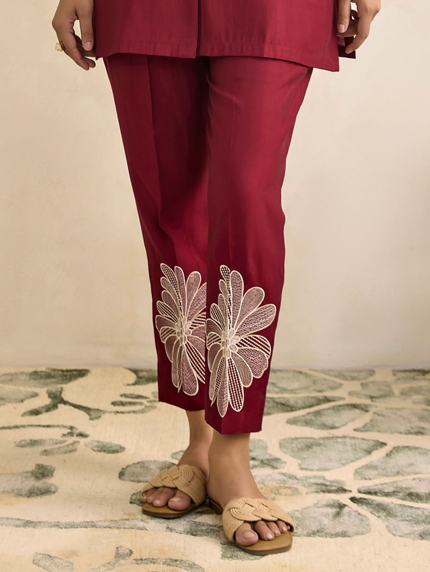 Maroon pants with floral embroidery on a neutral background
