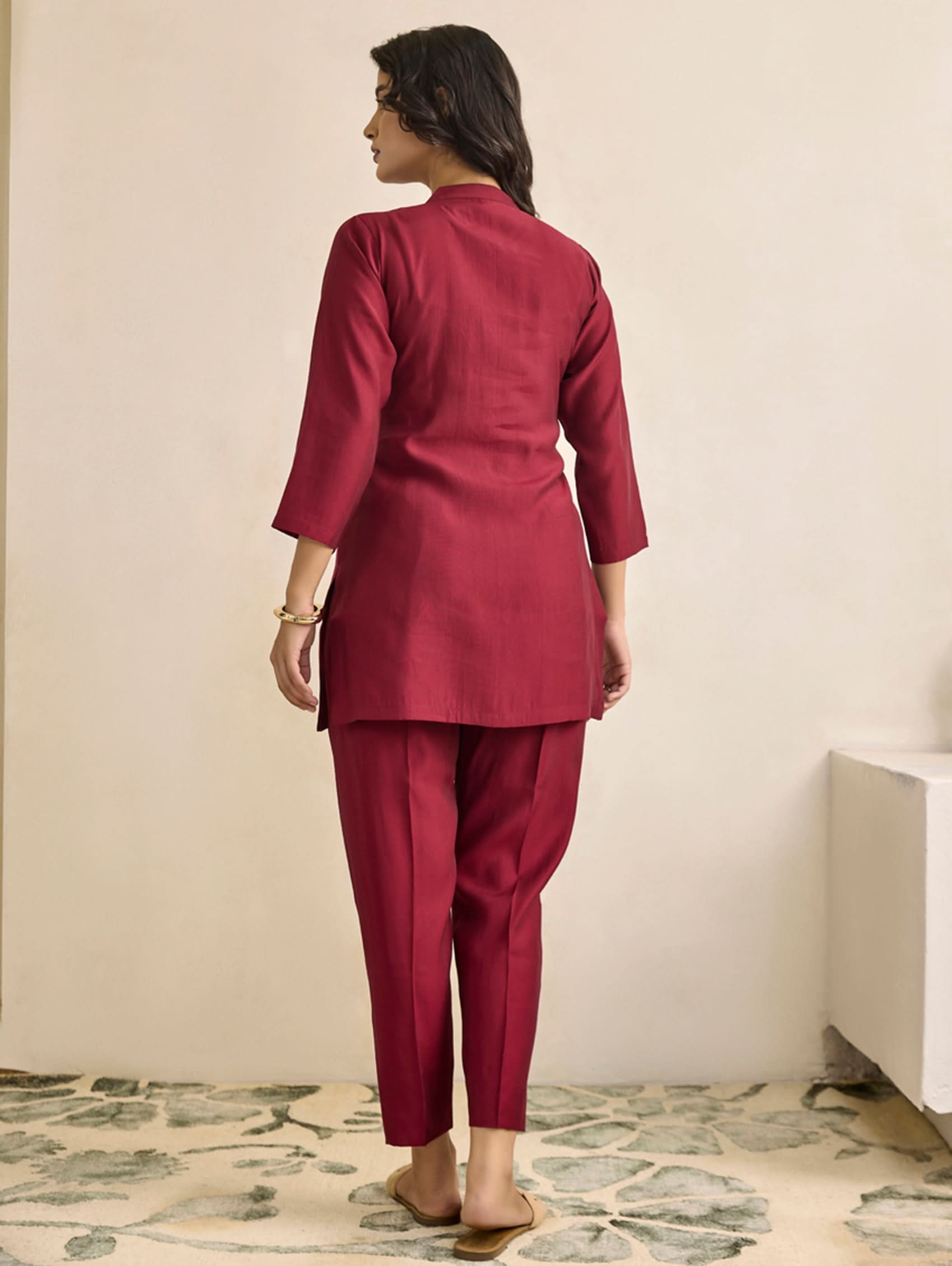 Person wearing a maroon outfit standing against a plain wall.