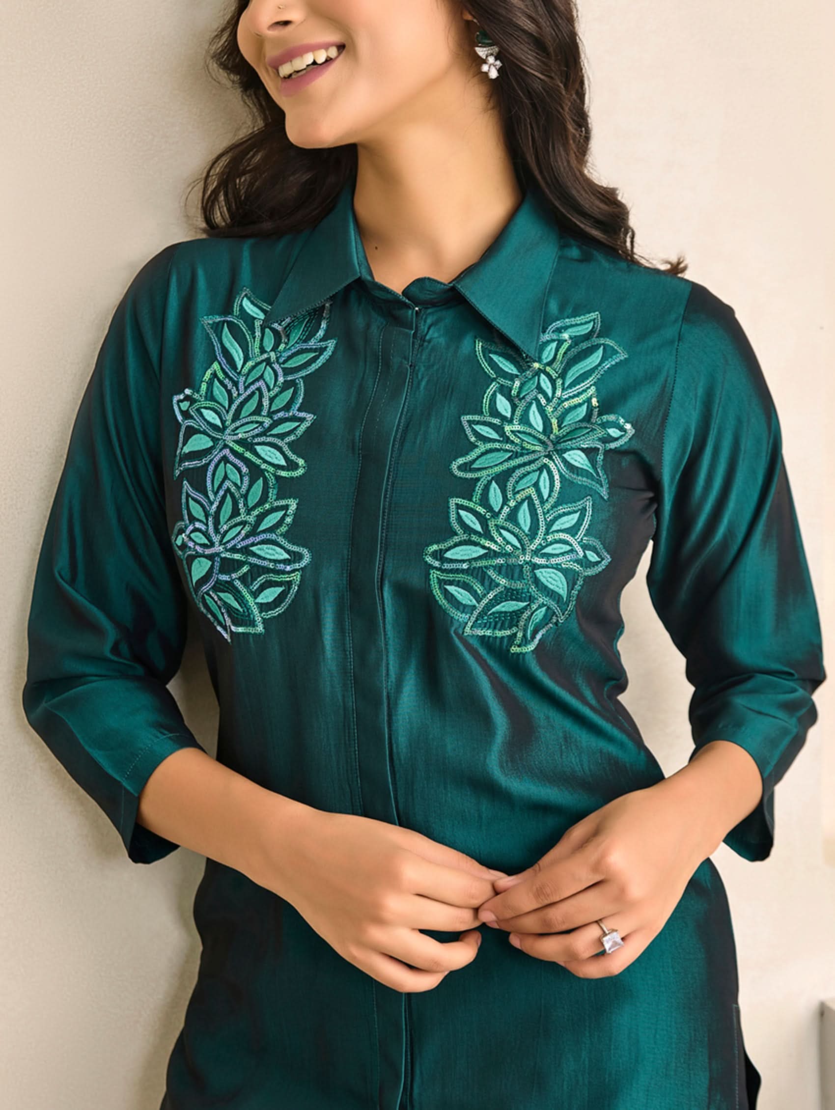 Woman wearing a green shirt with floral embroidery against a plain background