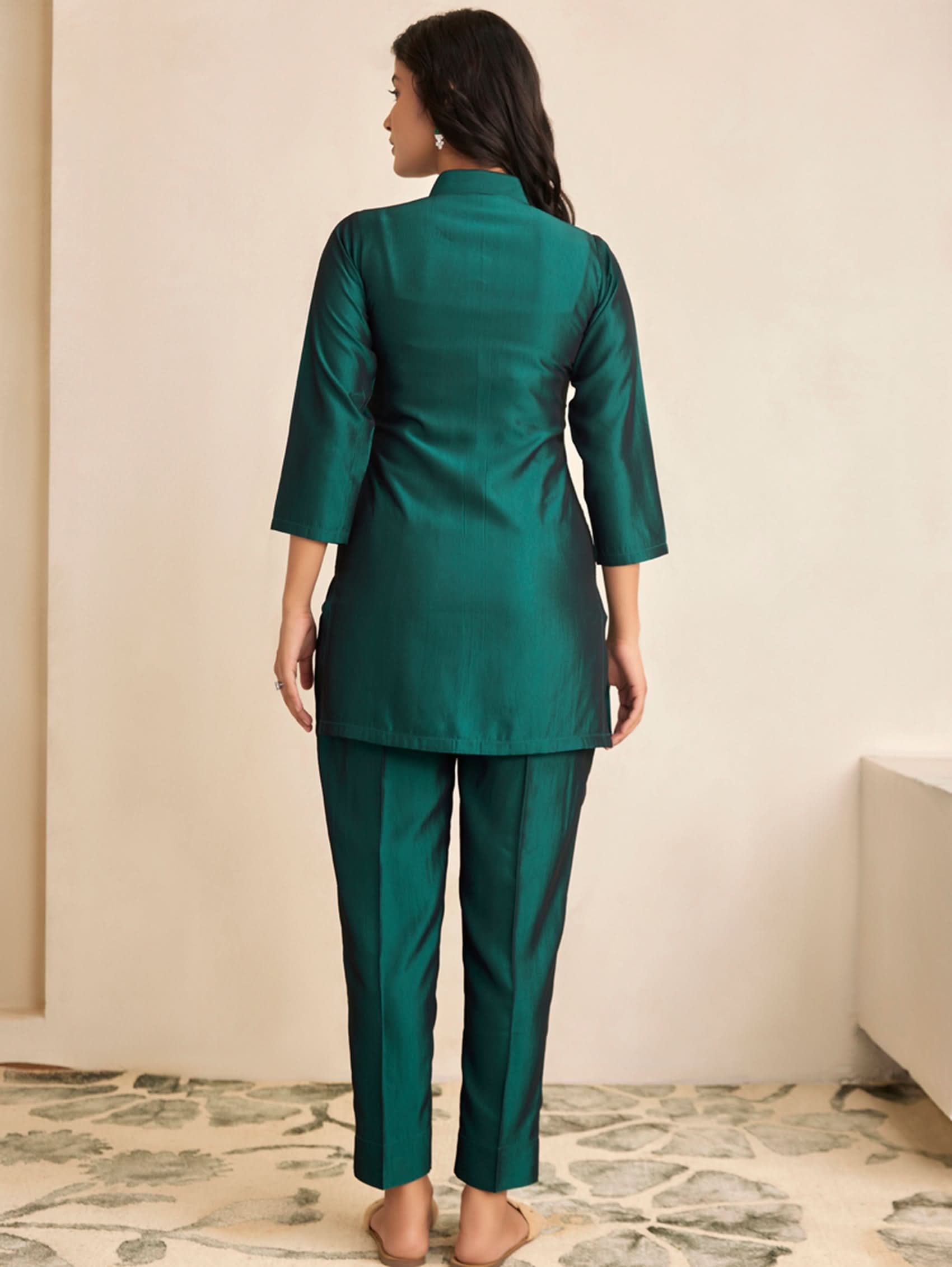 Woman wearing a green outfit standing in a room with a neutral background