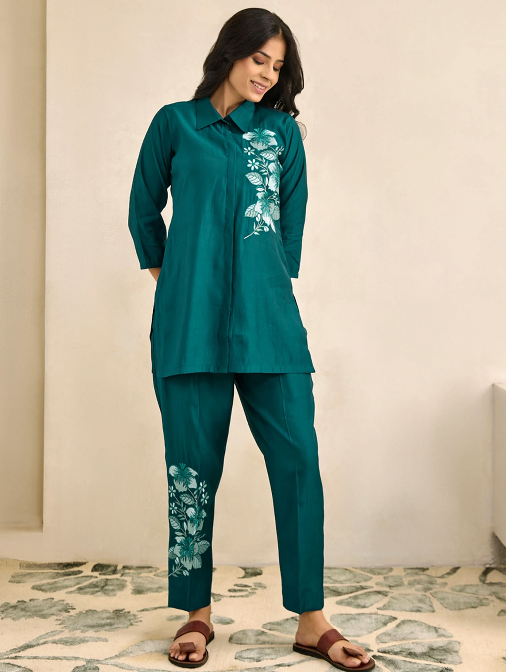 Woman wearing a teal outfit with floral patterns on a neutral background