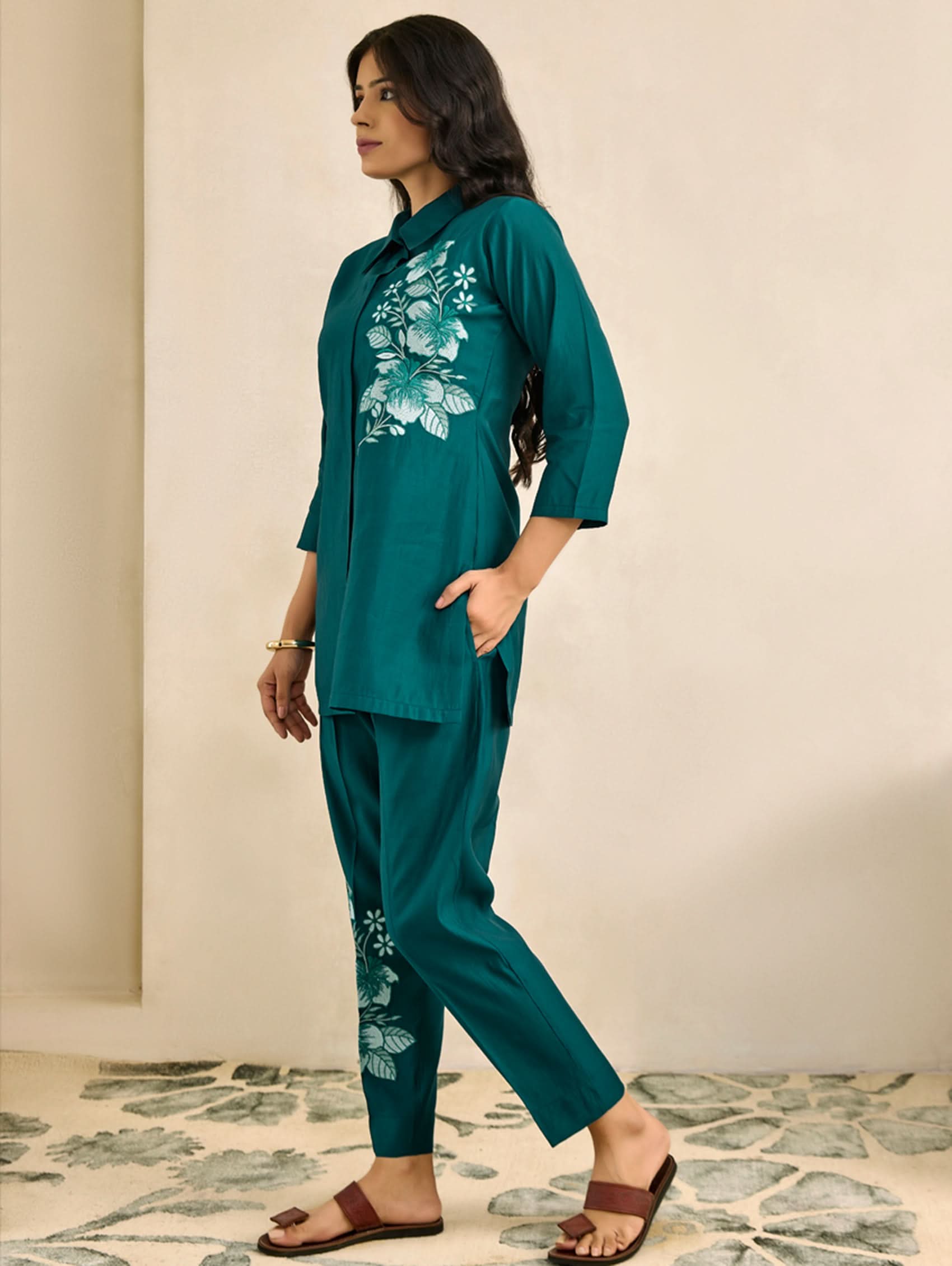 Woman wearing a teal outfit with floral patterns on a neutral background