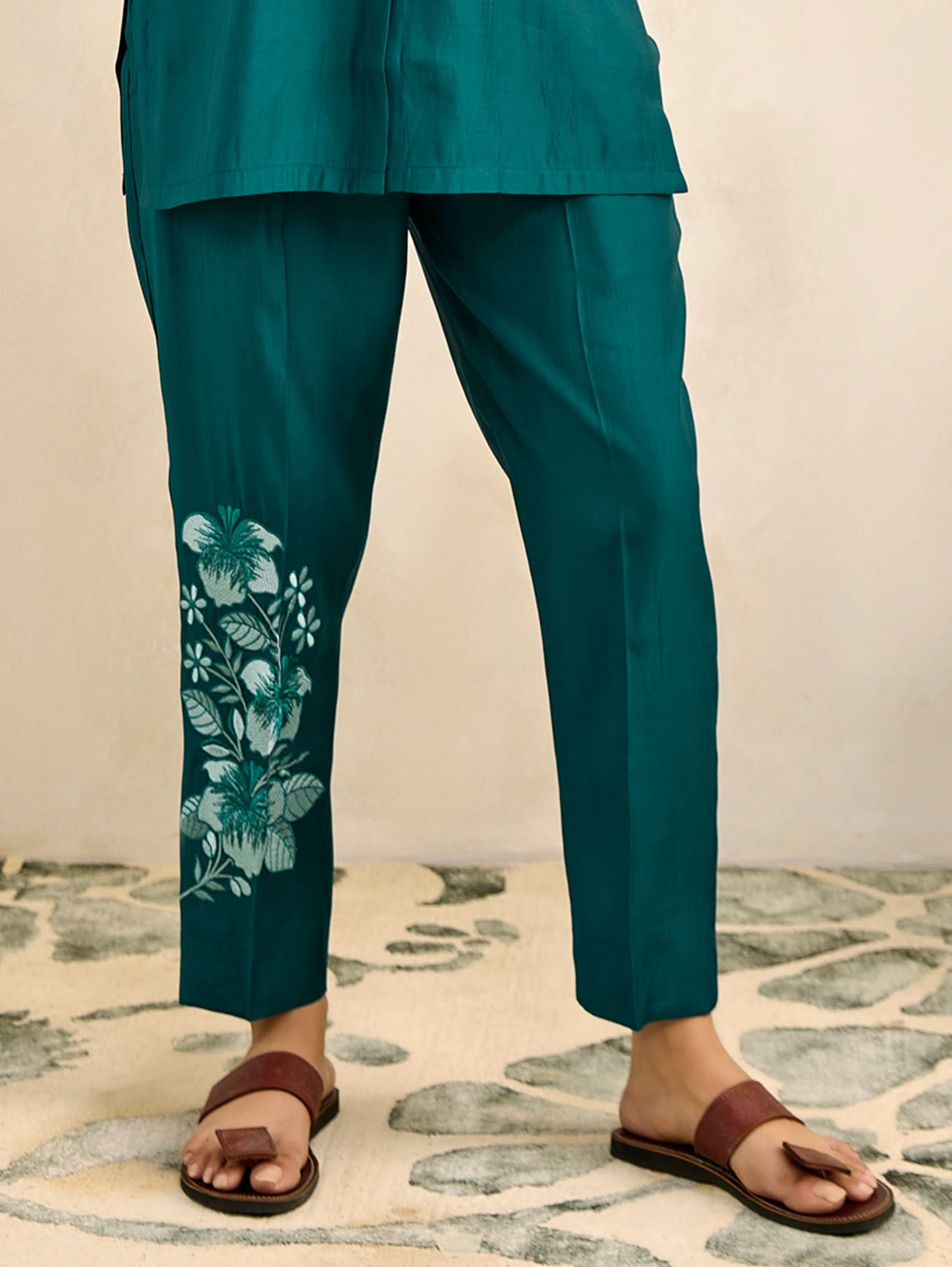Teal pants with floral embroidery on a patterned rug