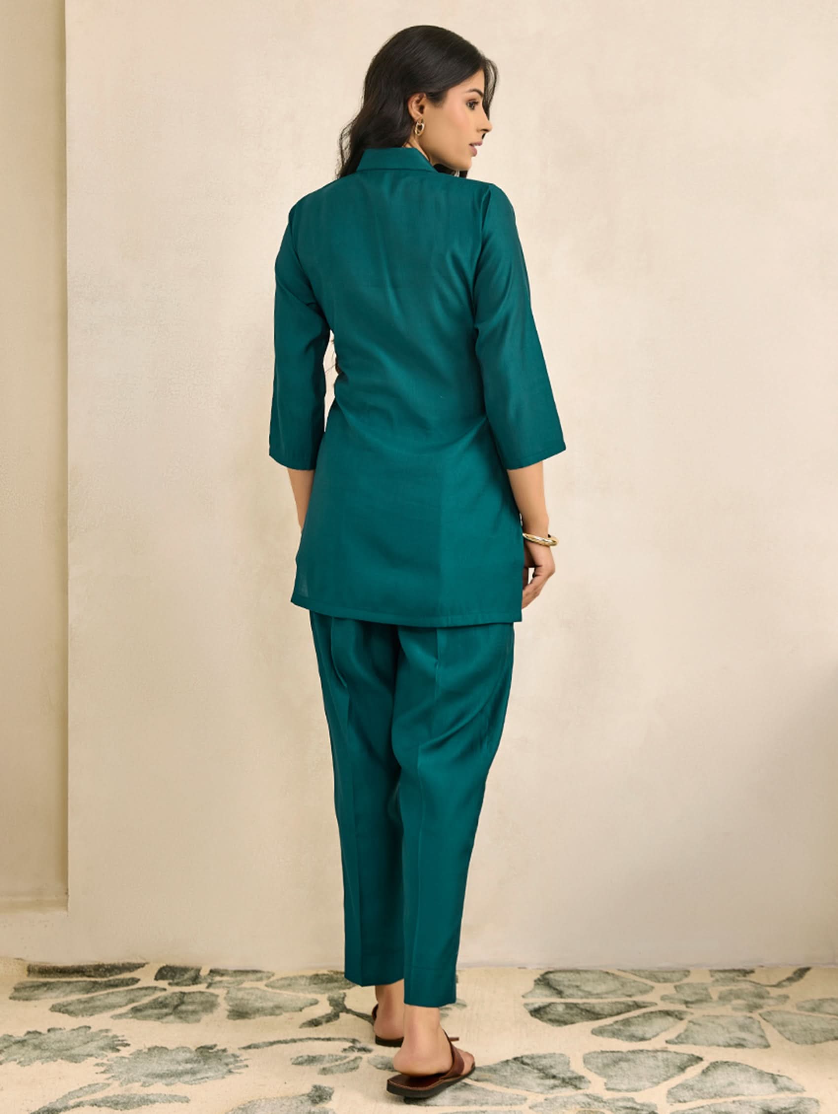 Woman wearing a teal suit standing against a beige wall.
