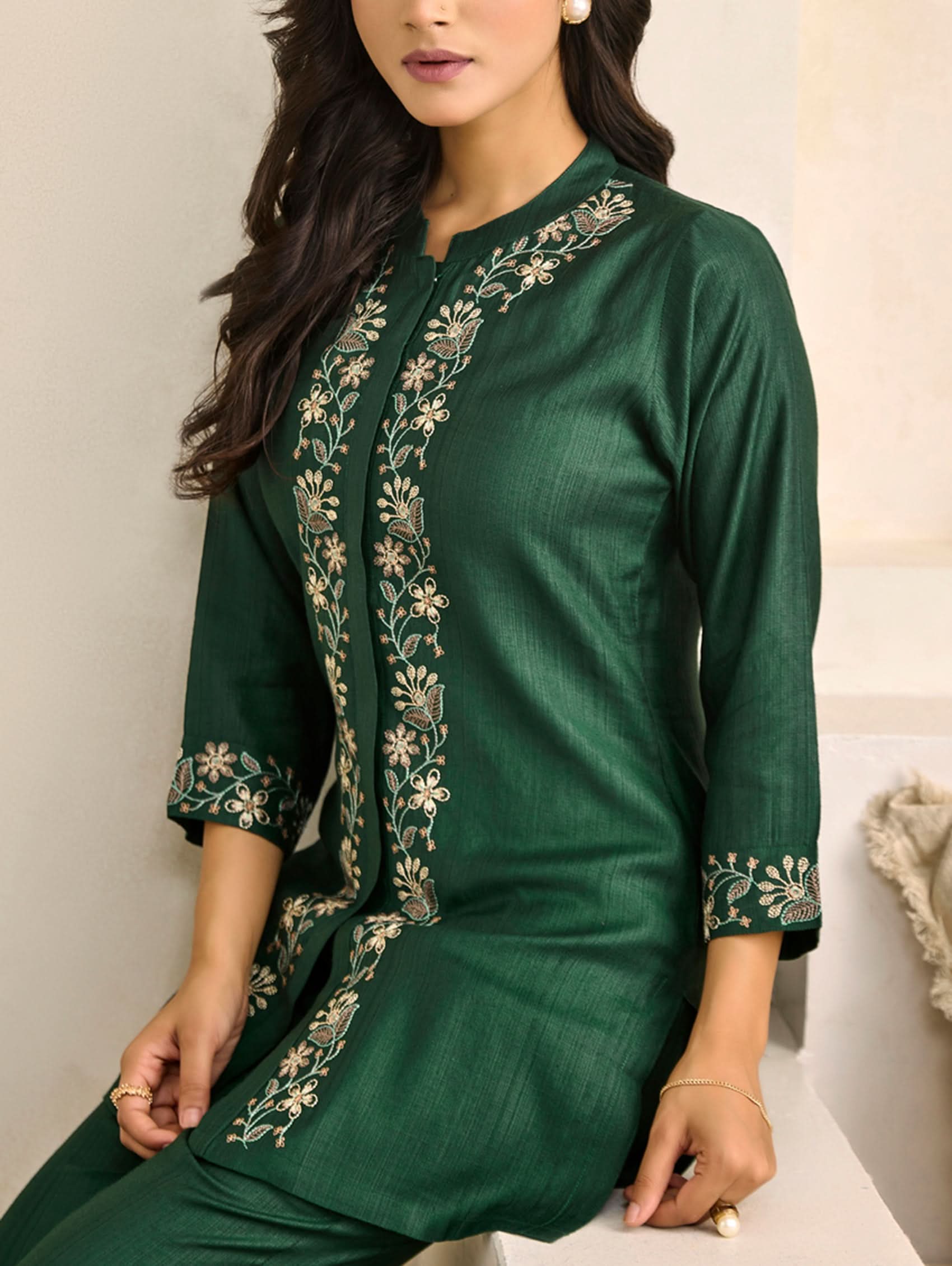 Woman wearing a green traditional outfit with floral embroidery on a neutral background