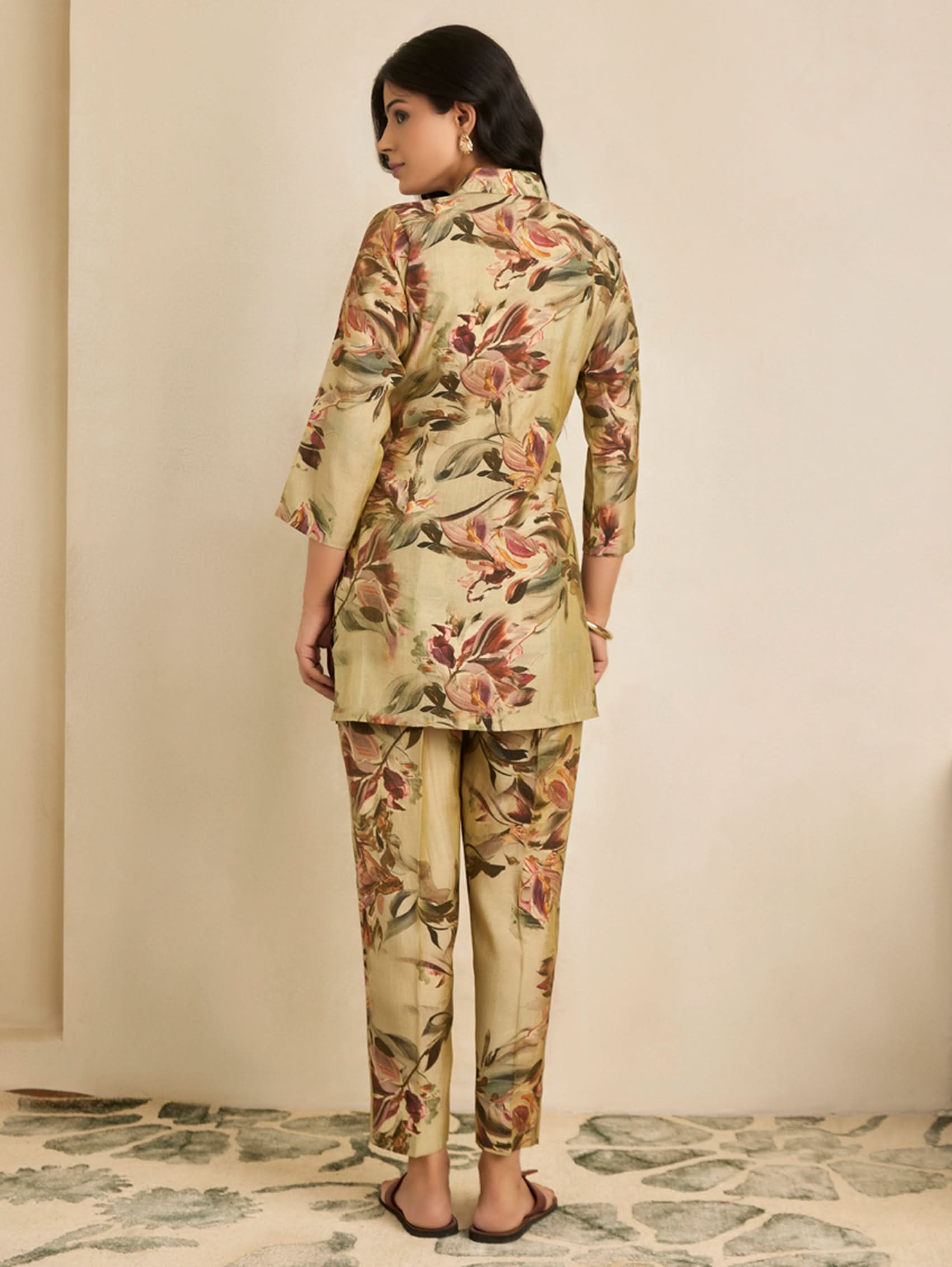 Woman wearing a floral outfit standing against a beige wall.