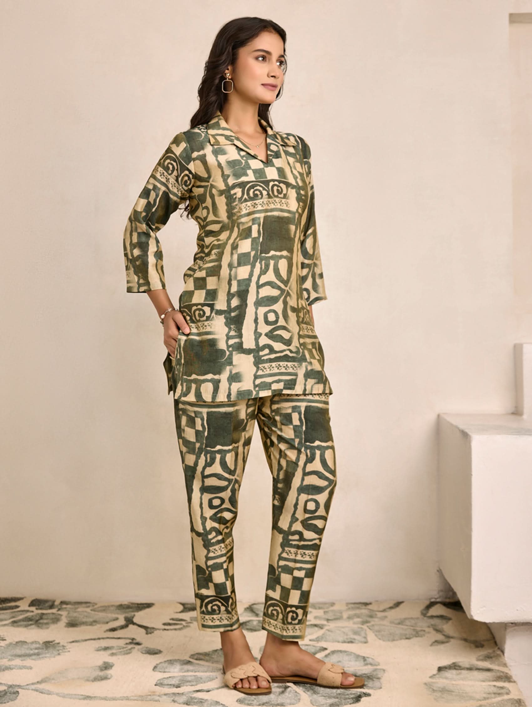 Woman wearing a green and beige patterned outfit in a minimalistic room.