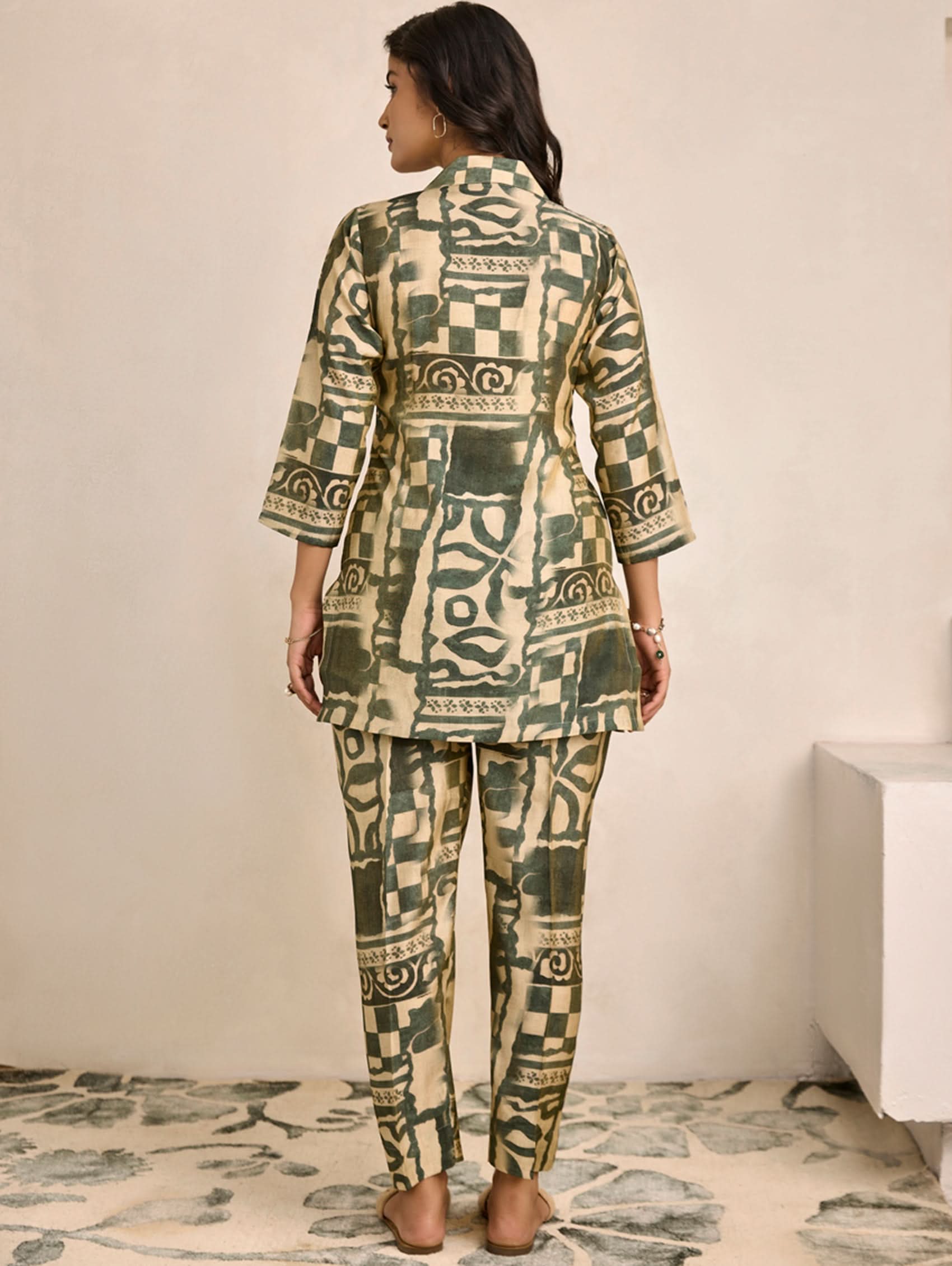 Woman wearing a patterned outfit standing in a minimalistic room.