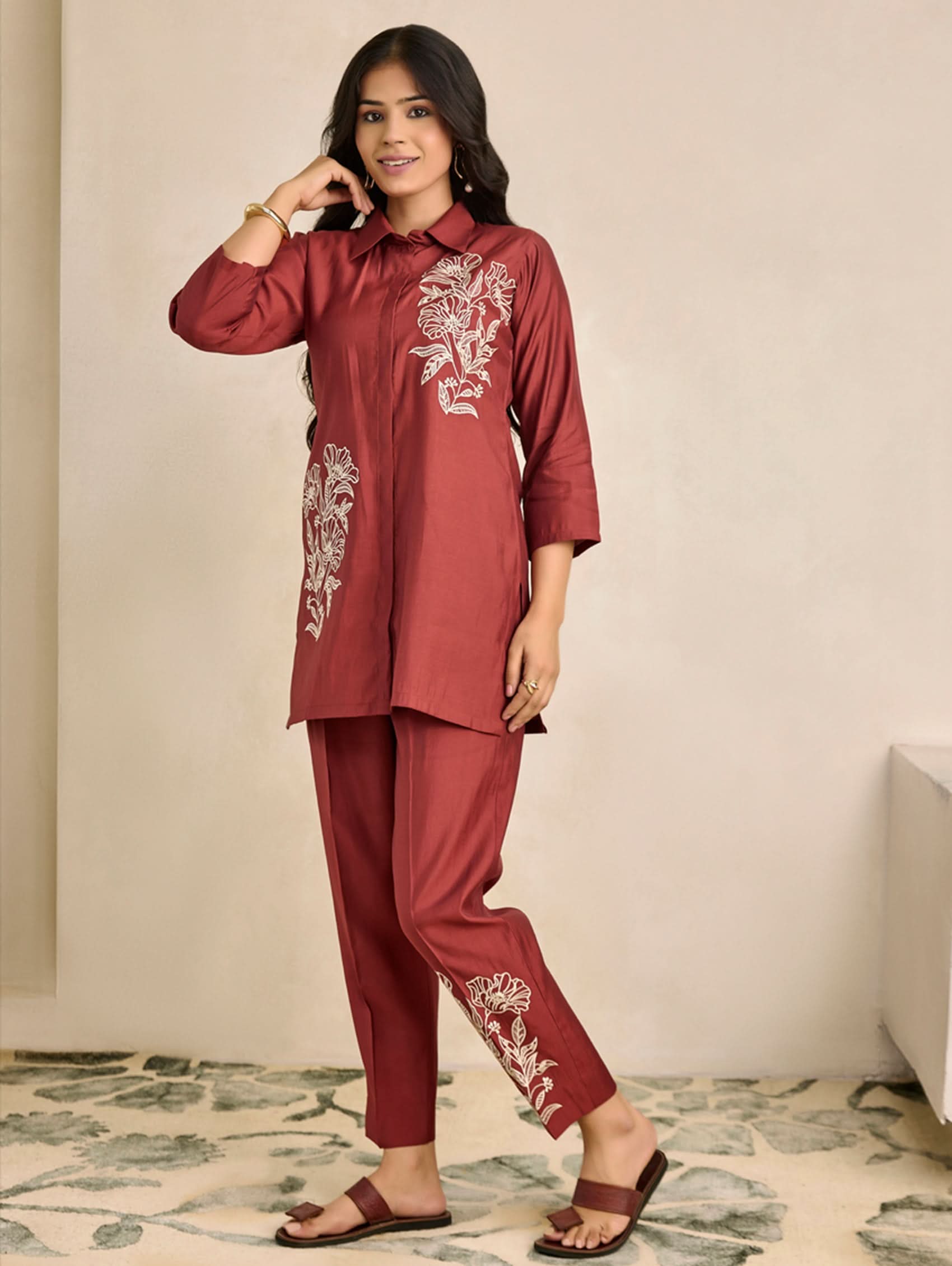 Woman wearing a maroon traditional outfit with floral embroidery on a neutral background