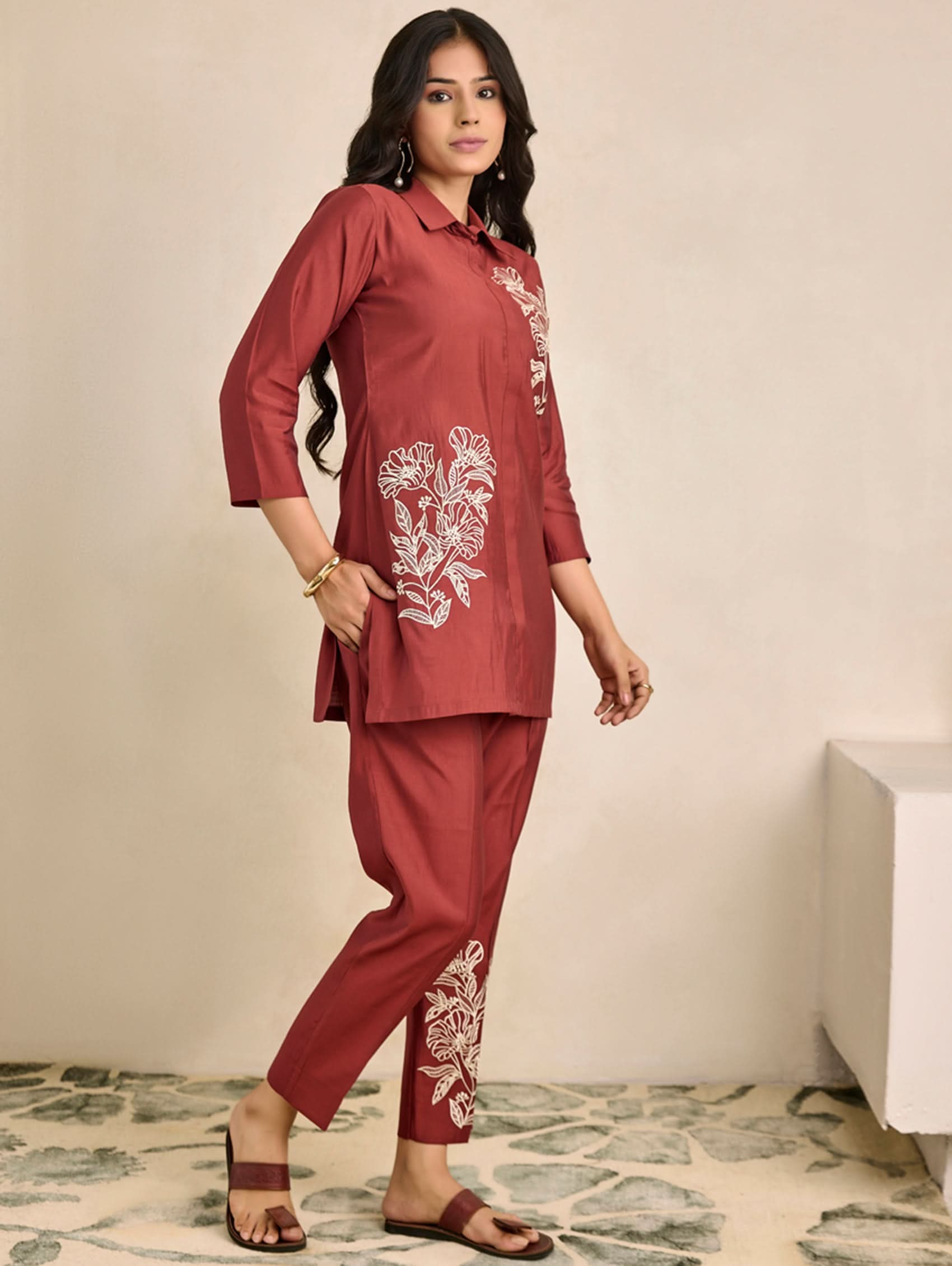 Woman wearing a red outfit with floral embroidery on a neutral background