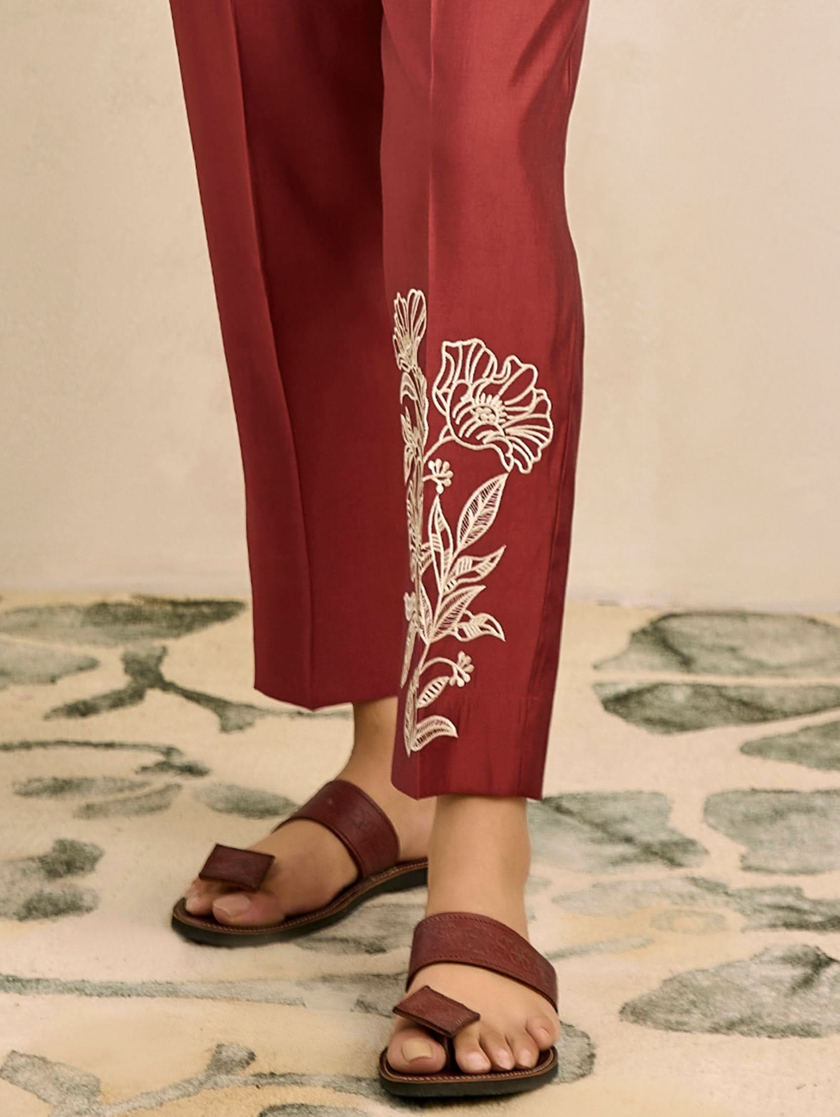 Red pants with white floral embroidery worn by a person on a patterned rug.