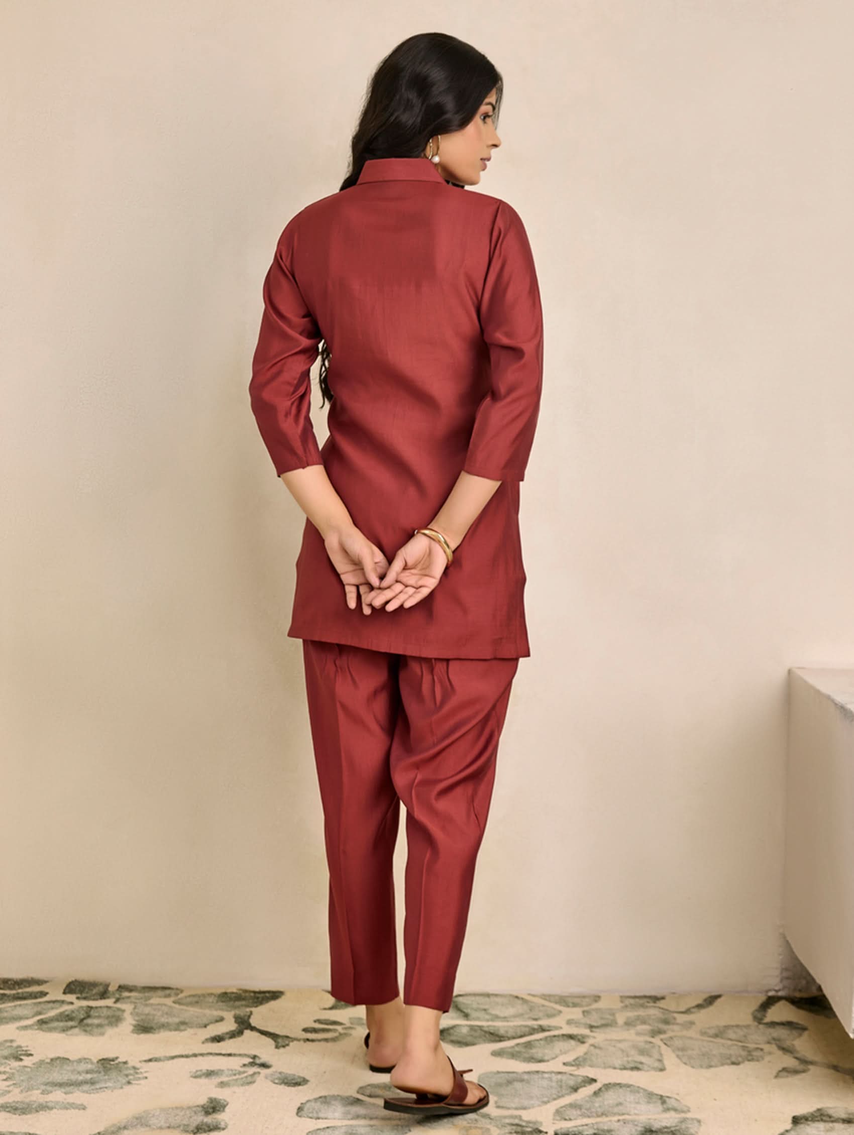 Woman wearing a red traditional outfit standing against a beige wall.