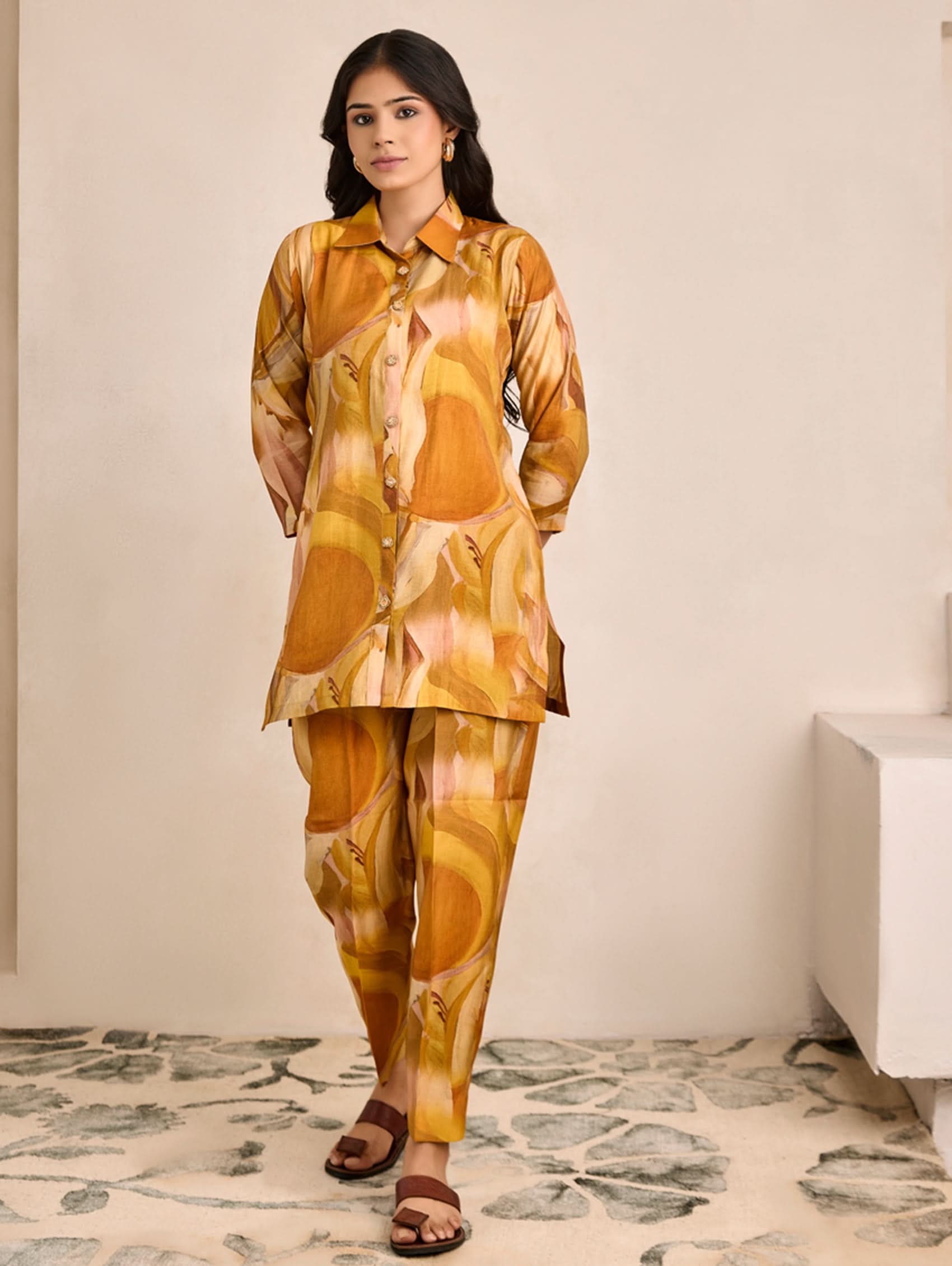 Woman wearing a yellow and brown patterned outfit standing in a room with a decorative floor.