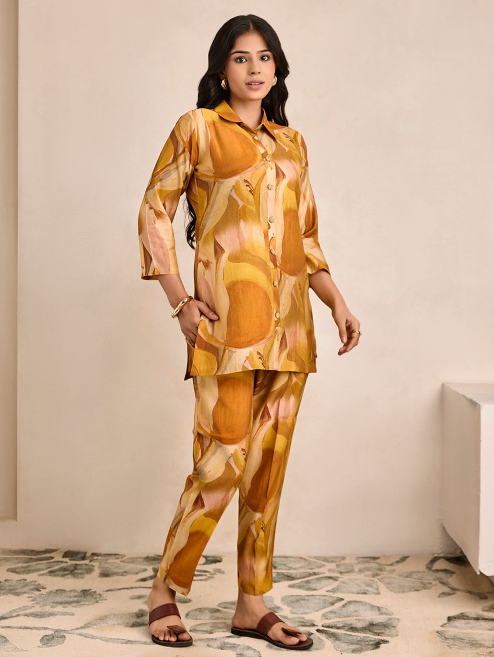 Woman wearing a yellow and orange patterned outfit standing in a room with a neutral background.