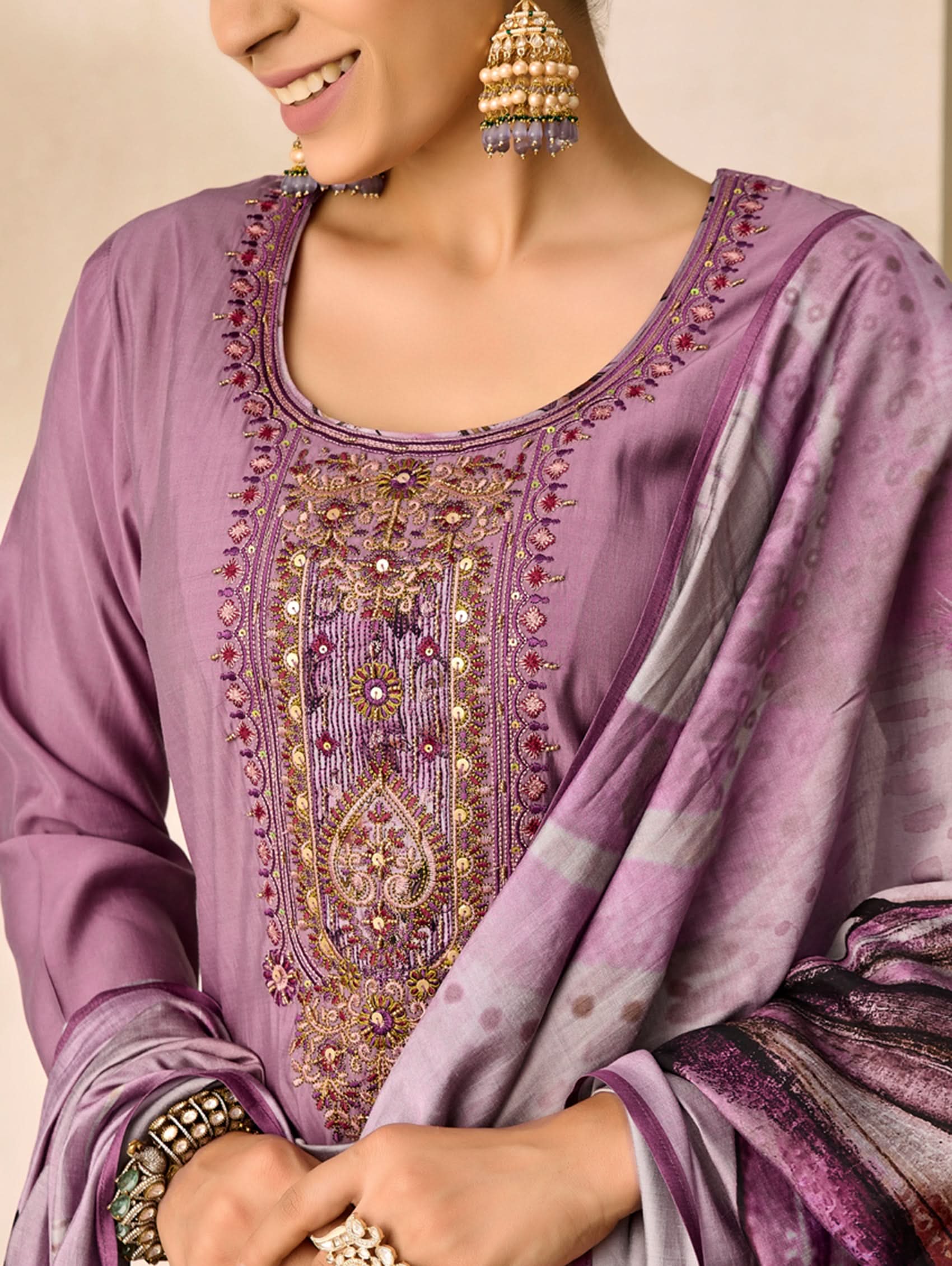 Woman wearing a purple embroidered traditional outfit with gold jewelry.