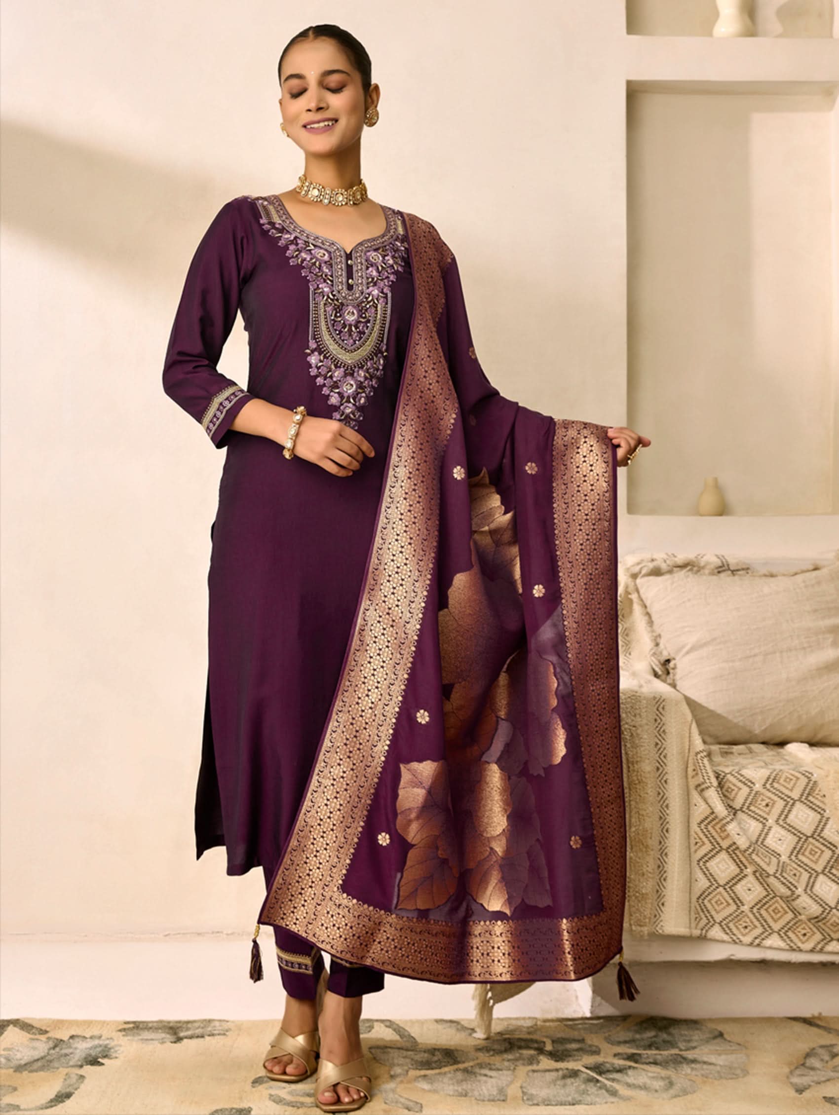 Woman wearing a purple traditional outfit with a matching dupatta in a living room setting.