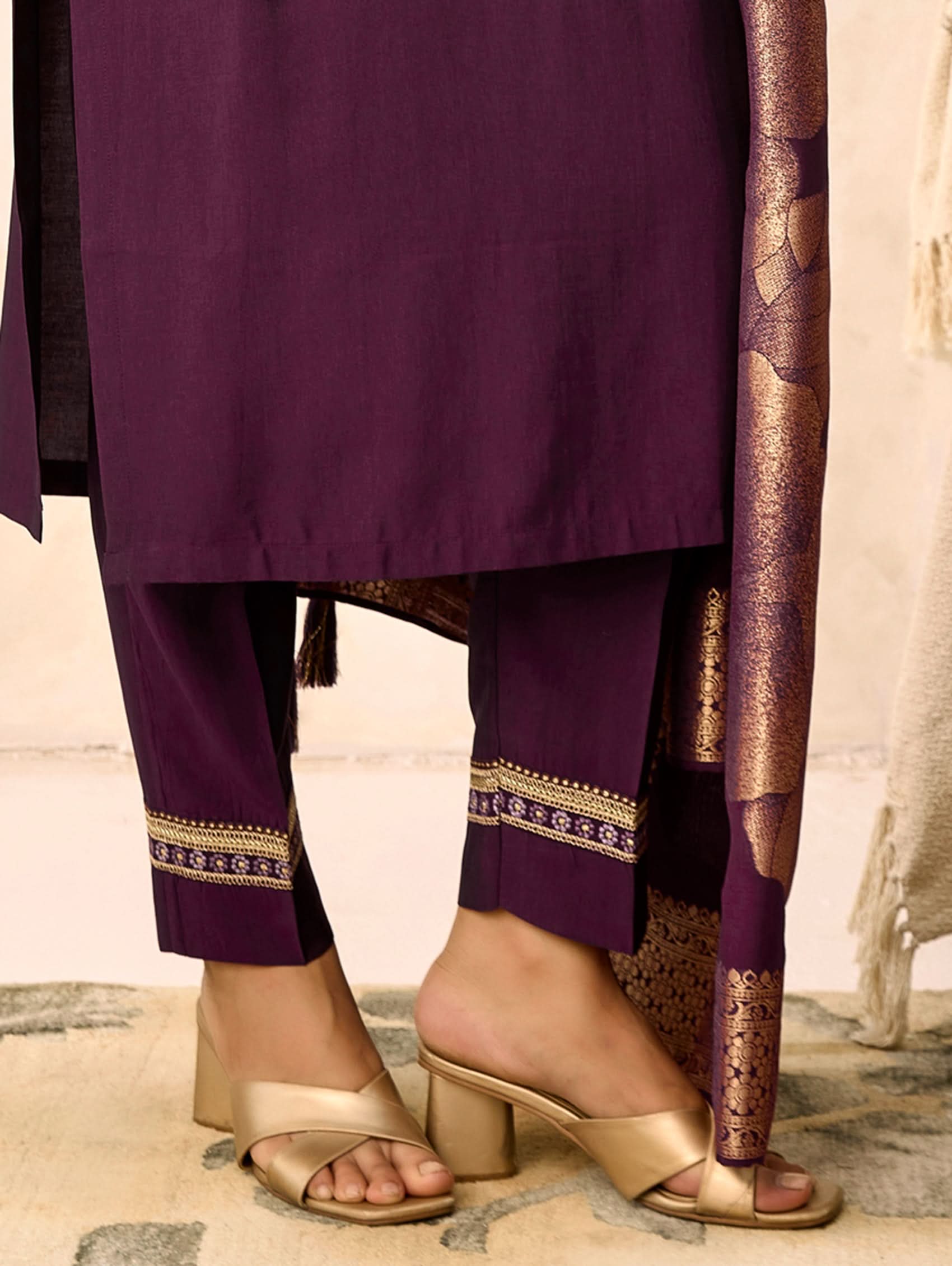Purple traditional outfit with gold embroidery and sandals on a neutral background