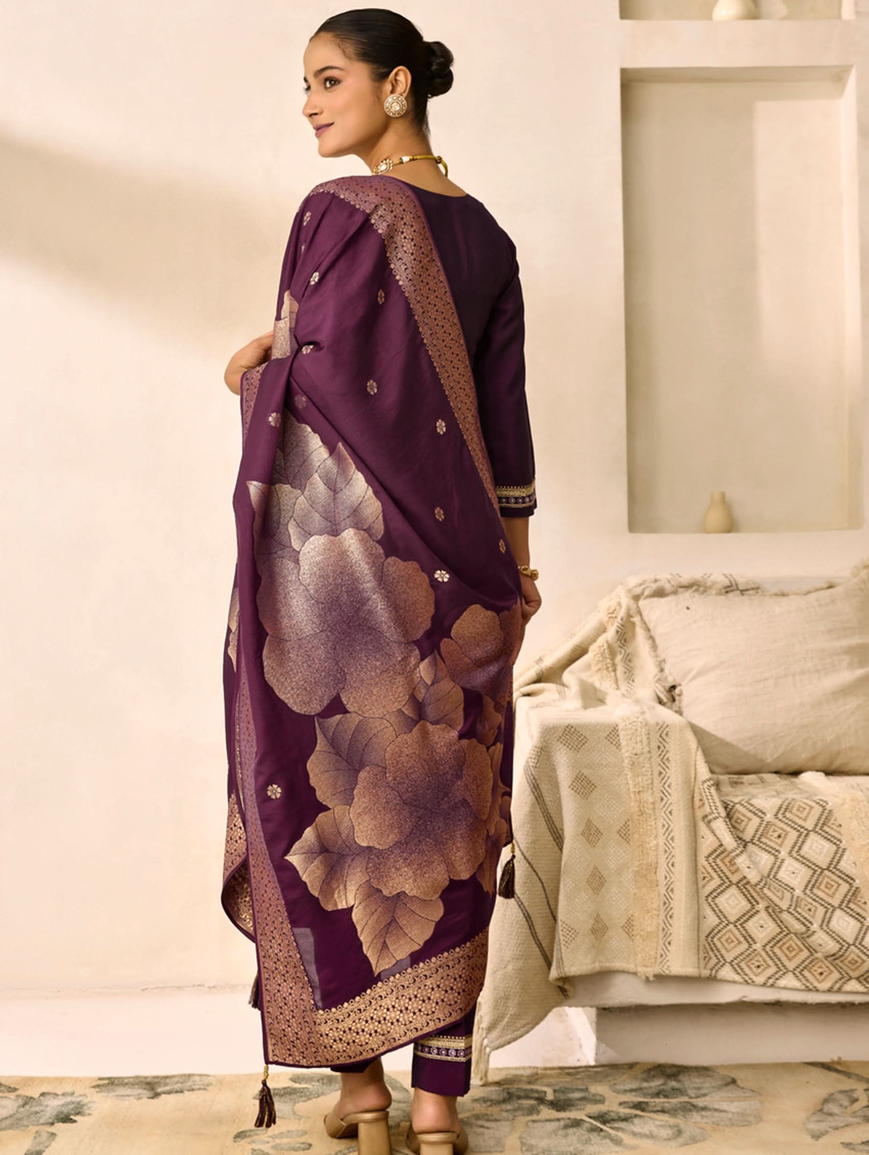 Woman wearing a purple saree with floral patterns in a room.
