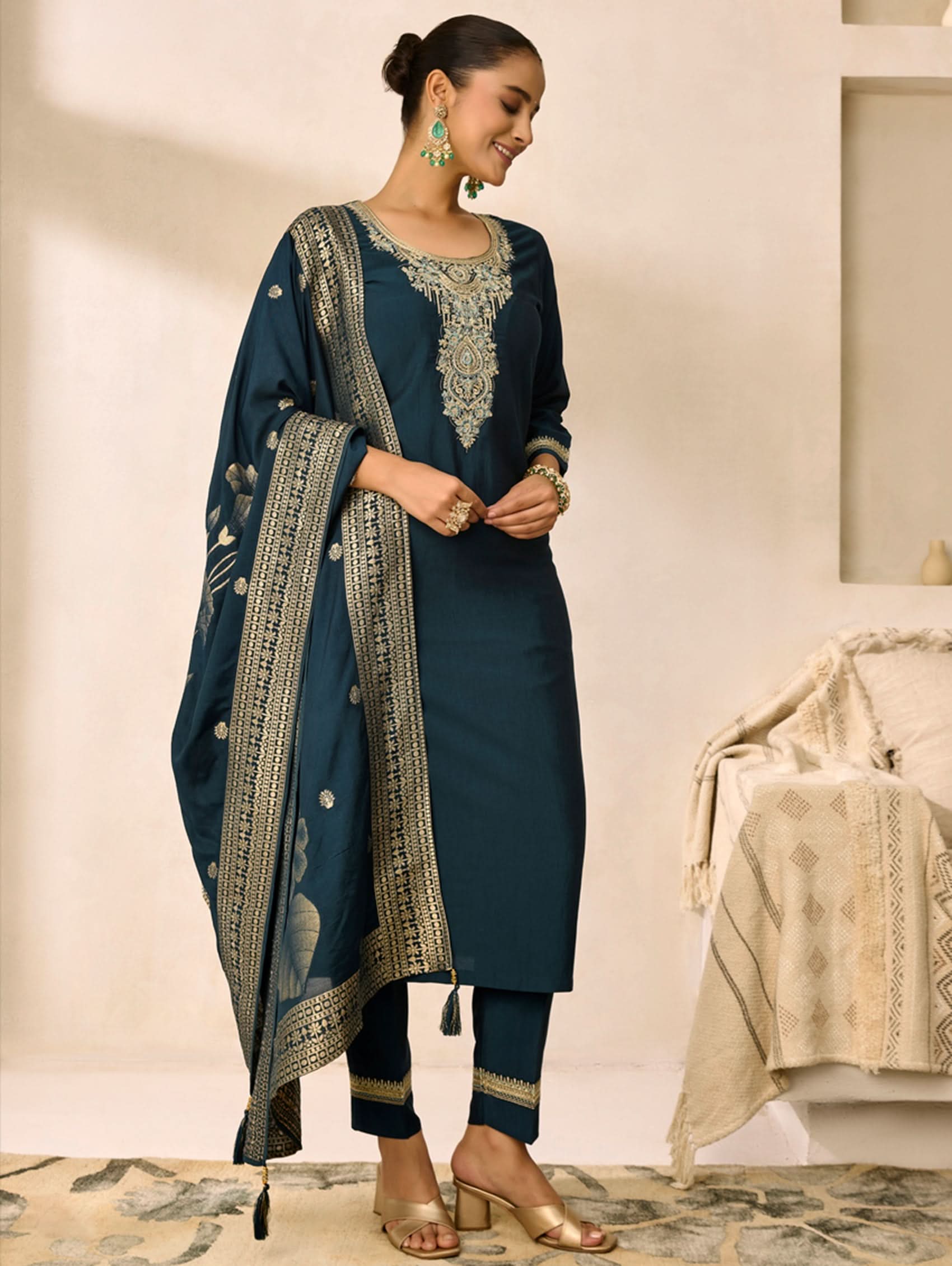 Woman in a blue traditional outfit with embroidery, standing in a minimalistic room.