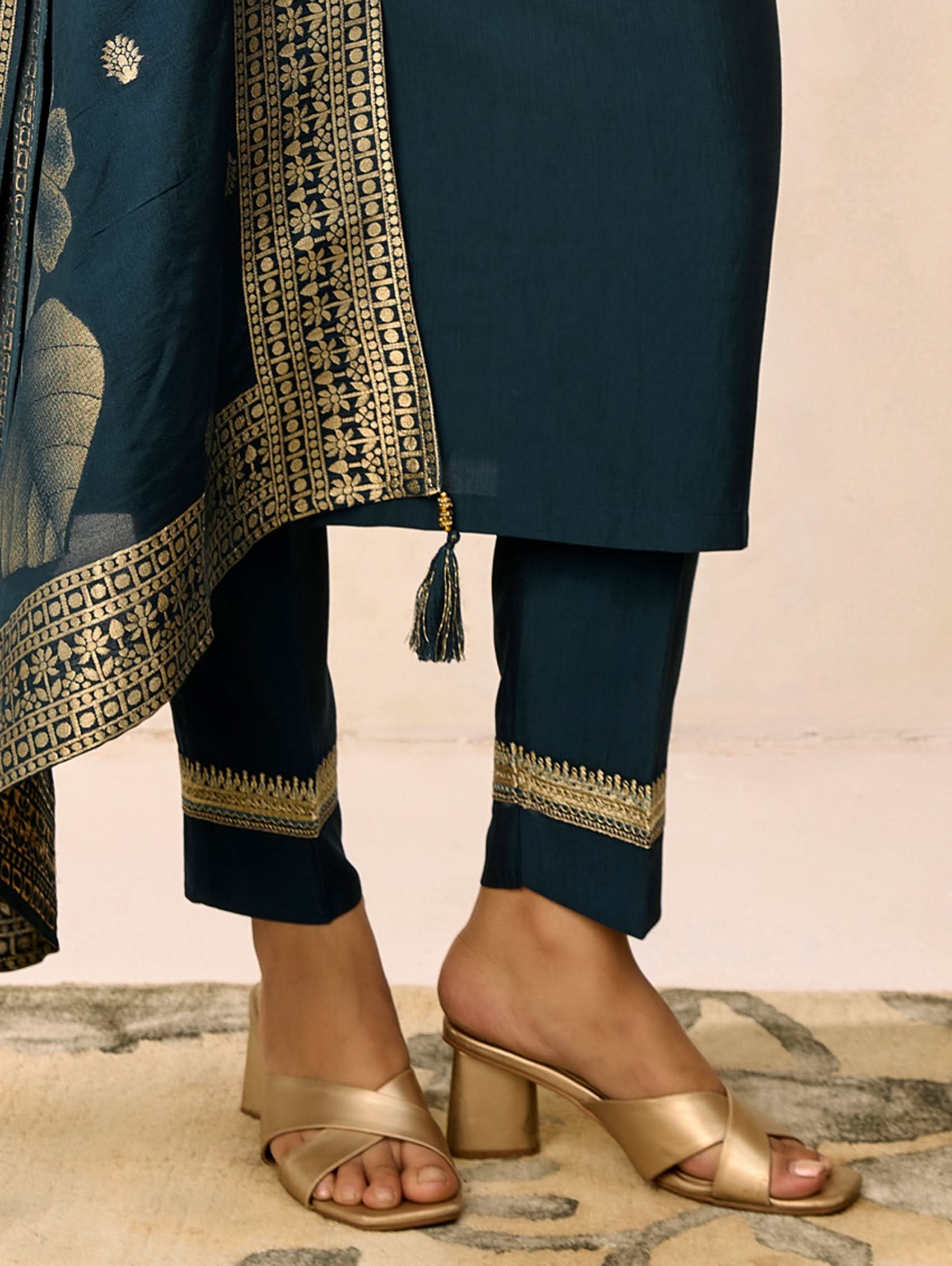 Navy blue traditional outfit with gold embroidery and gold sandals on a neutral background