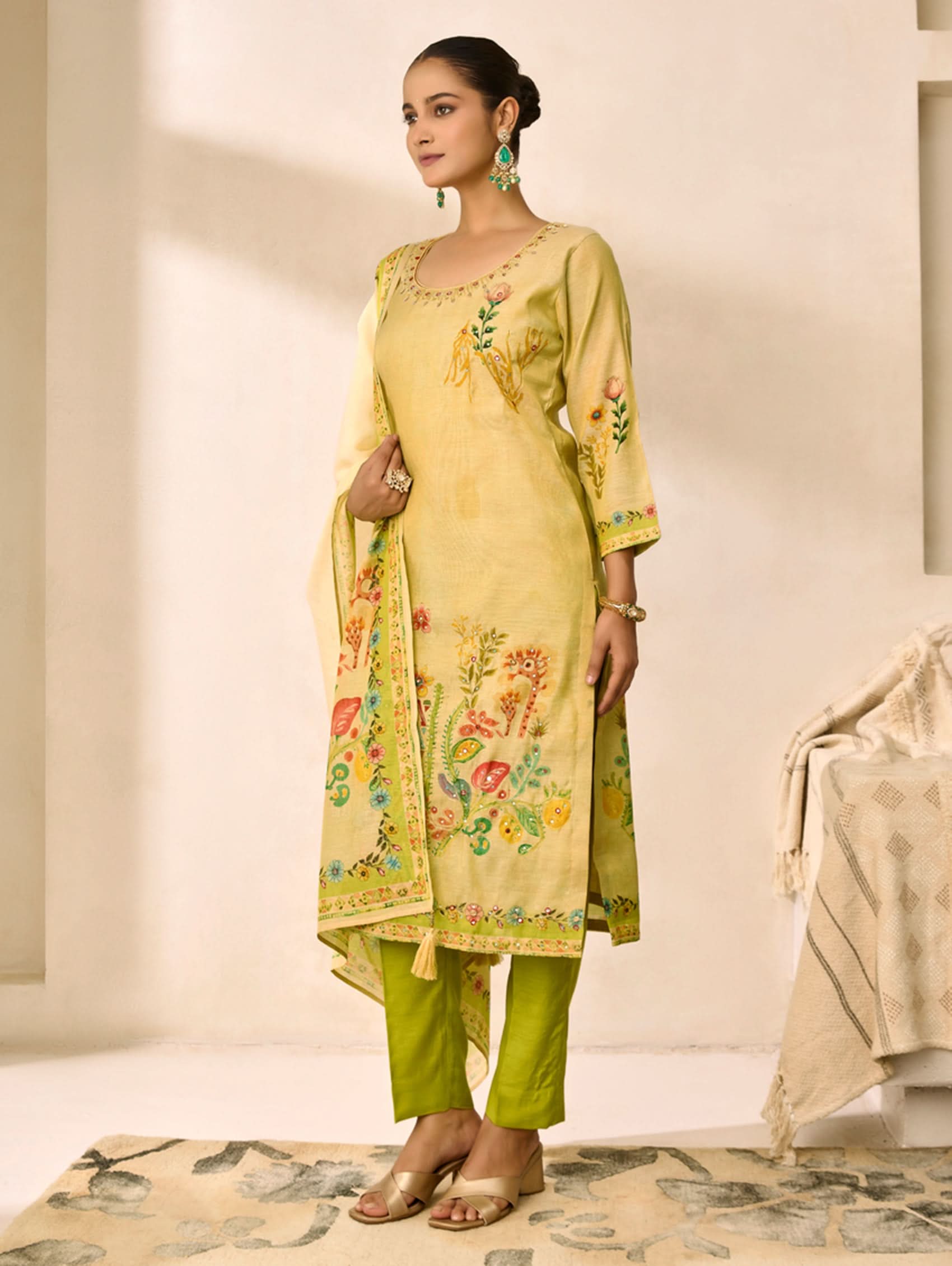Woman wearing a yellow embroidered outfit with green pants in a neutral setting