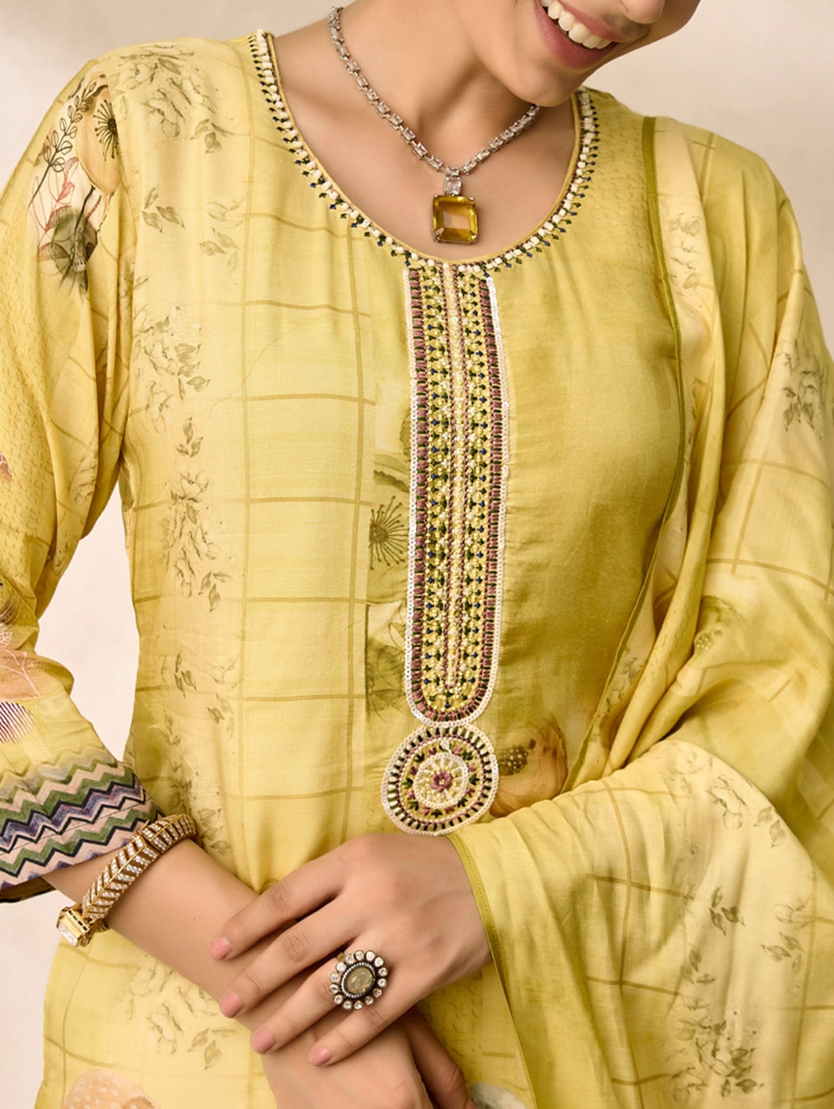 Yellow traditional outfit with intricate embroidery and jewelry on a plain background