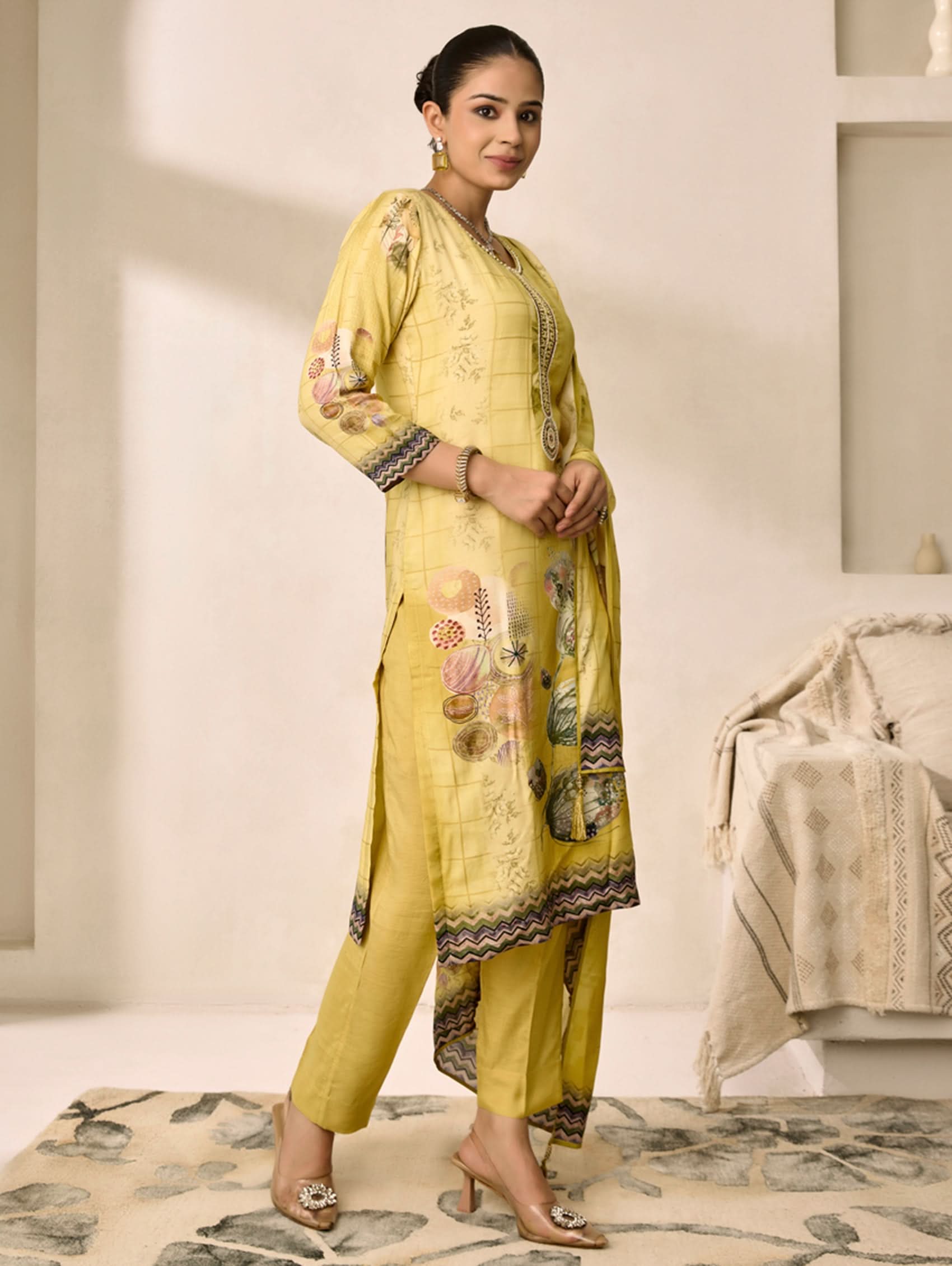 Woman wearing a yellow traditional outfit with floral patterns in a minimalistic room.