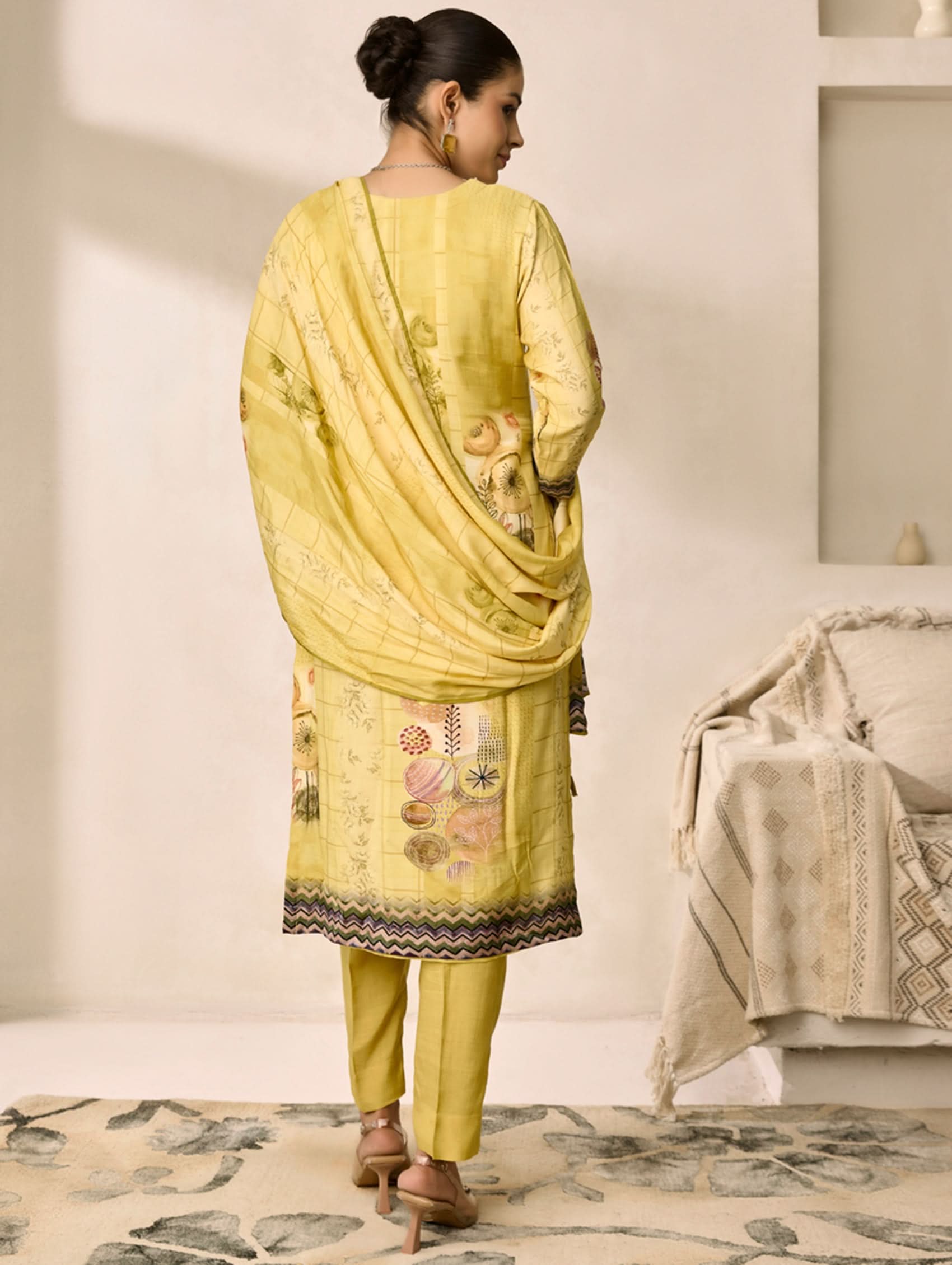 Woman wearing a yellow traditional outfit with a matching dupatta in a minimalistic room.