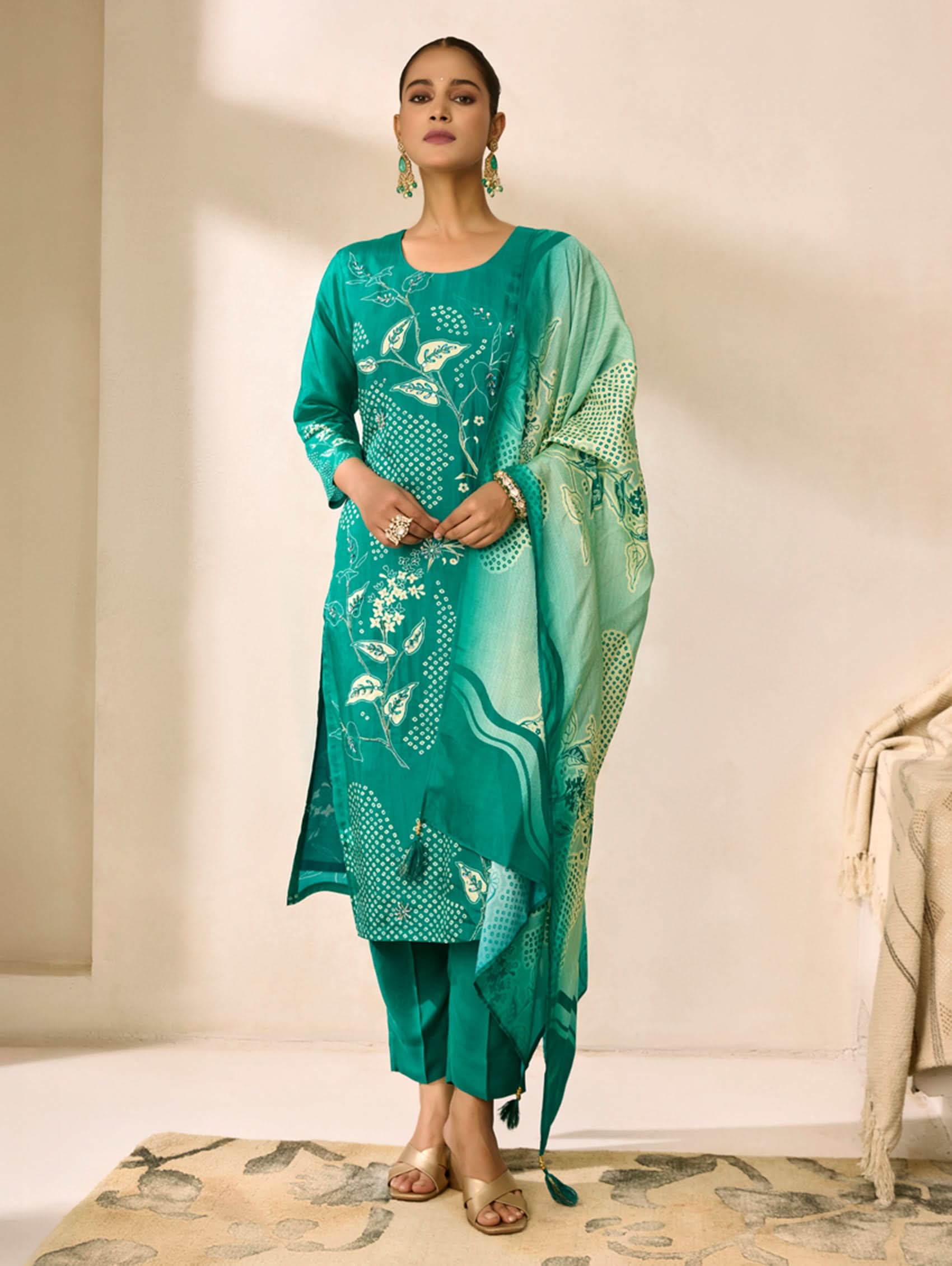 Woman wearing a green traditional outfit with floral patterns in a minimalistic setting.