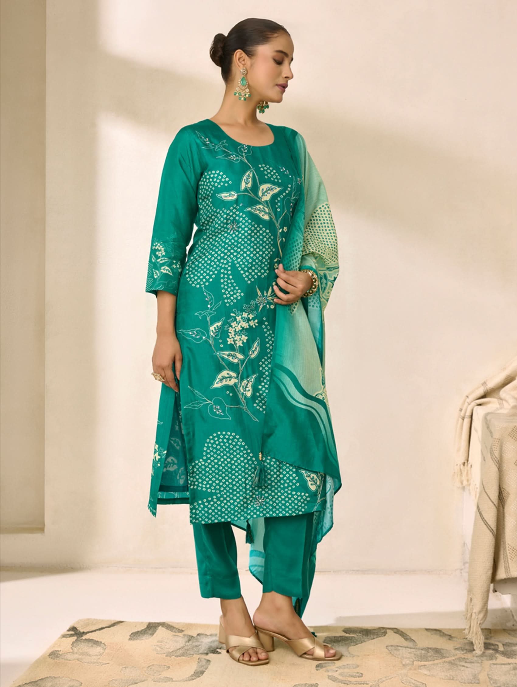 Woman wearing a teal traditional outfit with floral patterns in a neutral setting