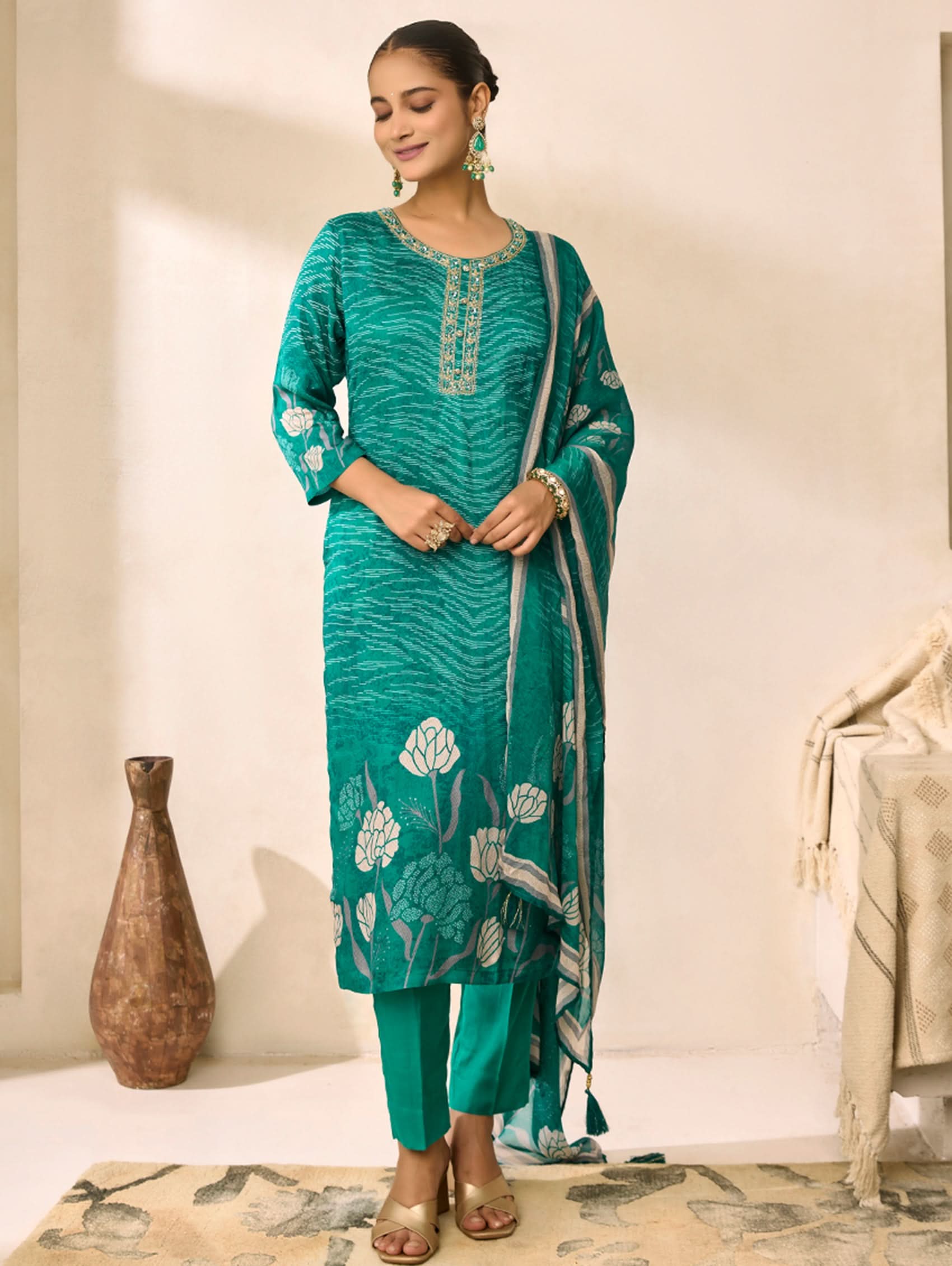 Woman wearing a teal traditional outfit with floral patterns in a minimalistic setting.