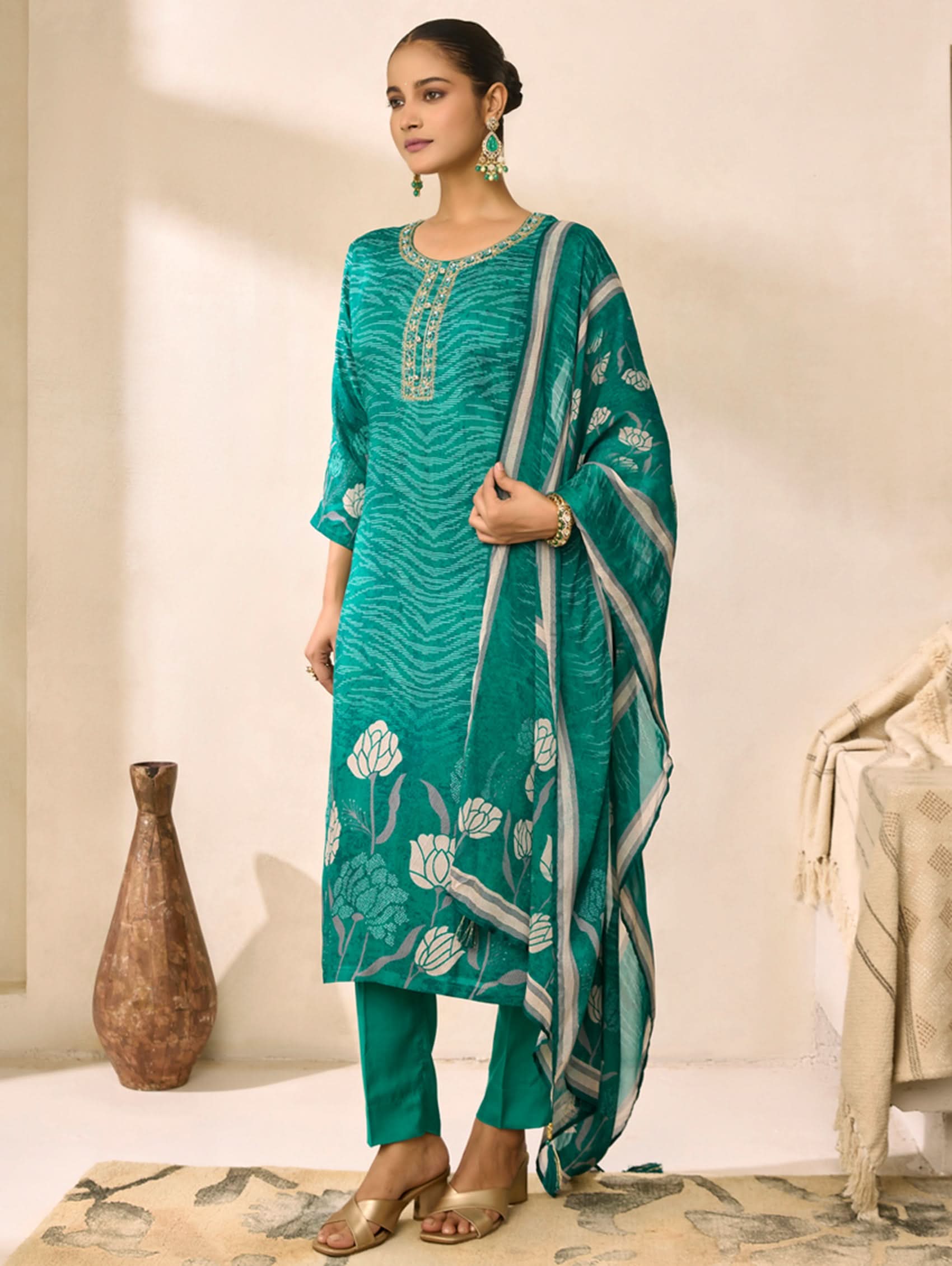Woman wearing a teal traditional outfit with a matching dupatta in a minimalistic setting.