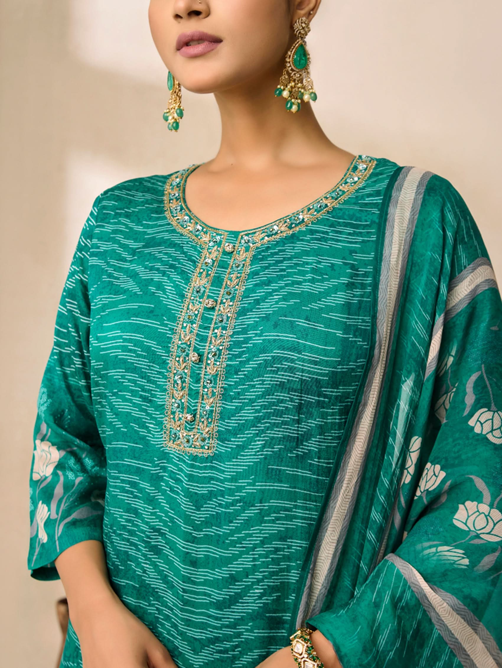 Woman wearing a green traditional outfit with intricate embroidery and matching earrings.
