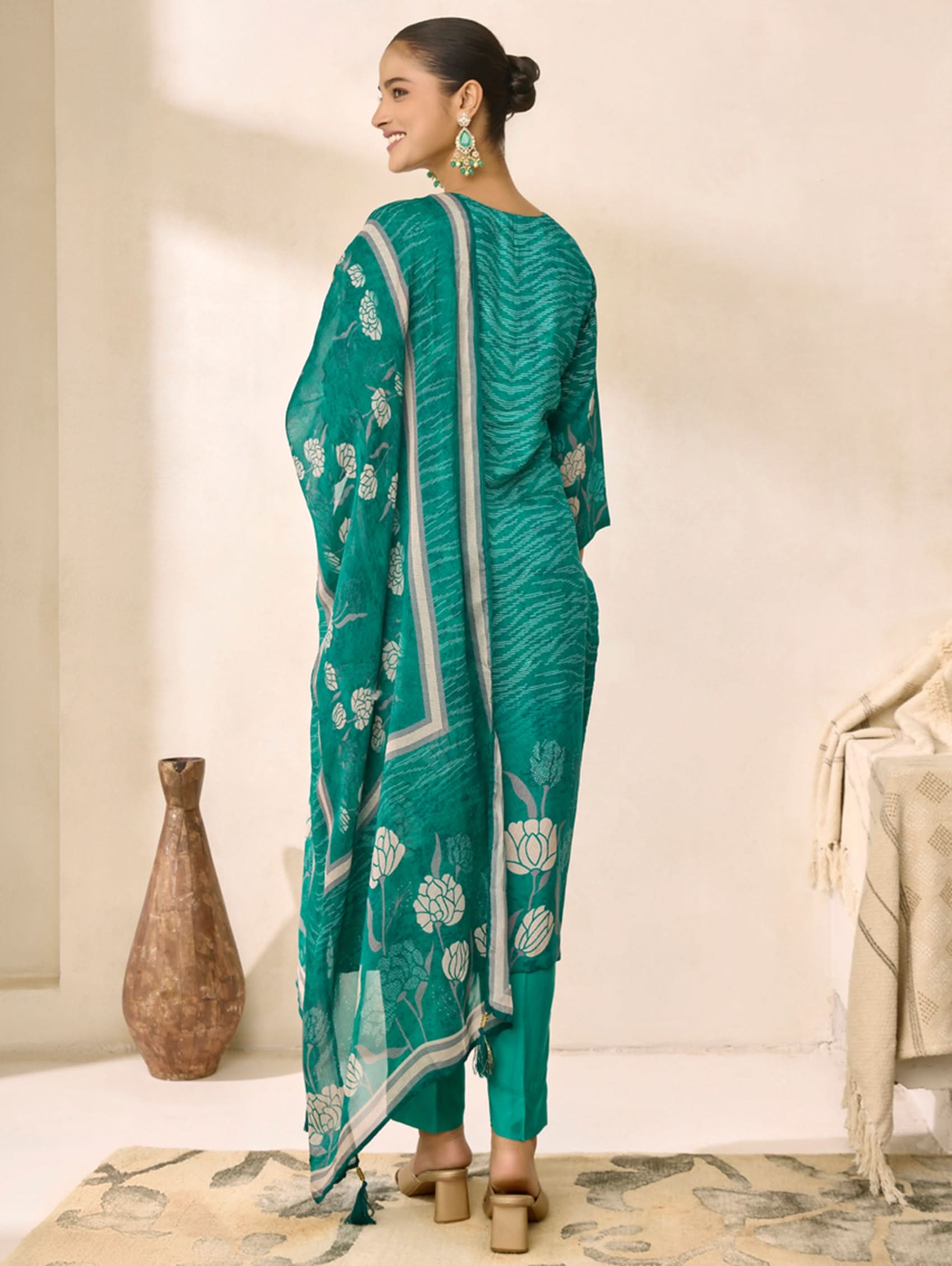Woman wearing a green saree with white floral patterns in a minimalistic setting.
