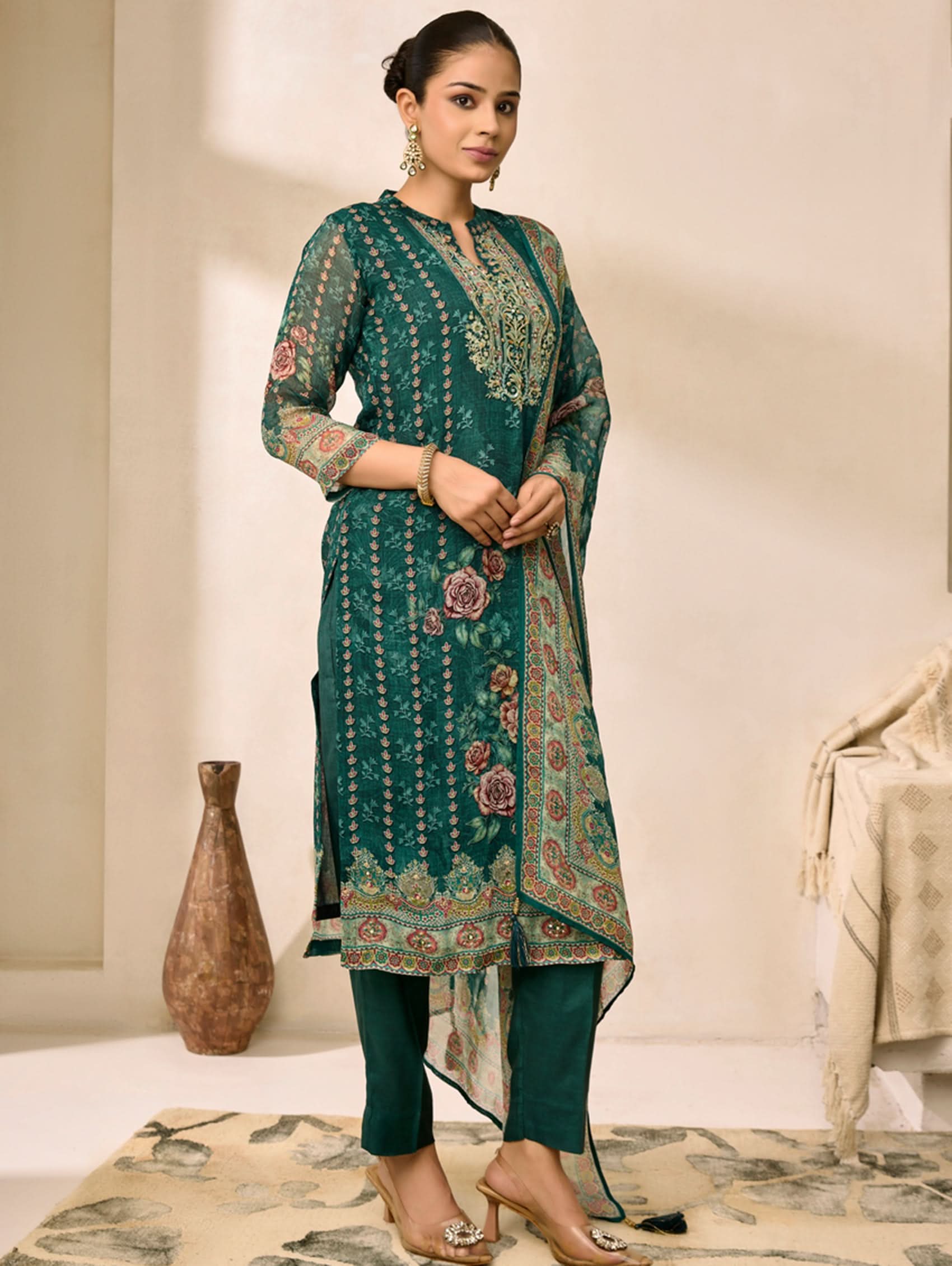 Woman wearing a green embroidered traditional outfit in a minimalistic room.