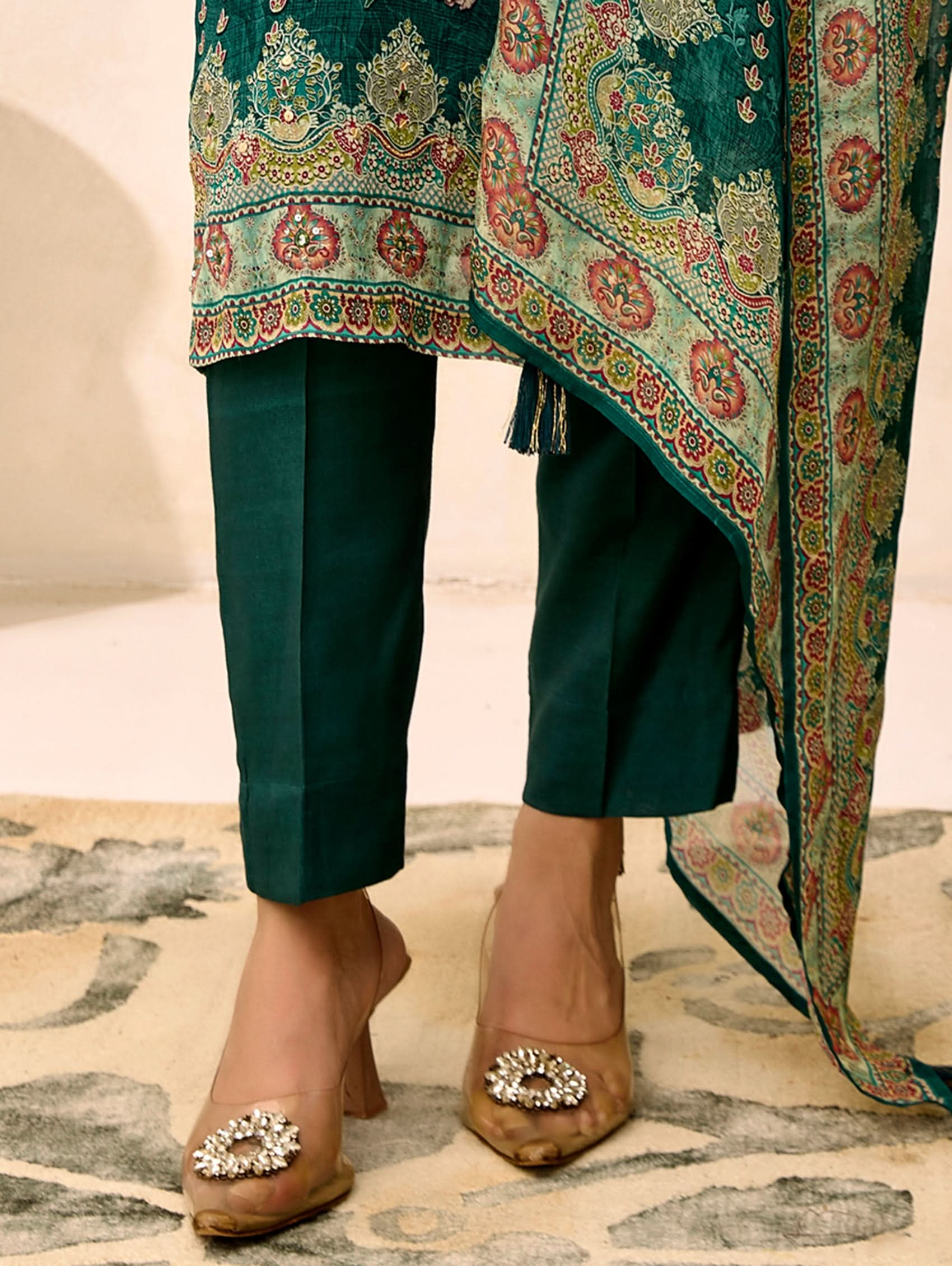 Green embroidered outfit with matching pants and brown shoes on a patterned rug.