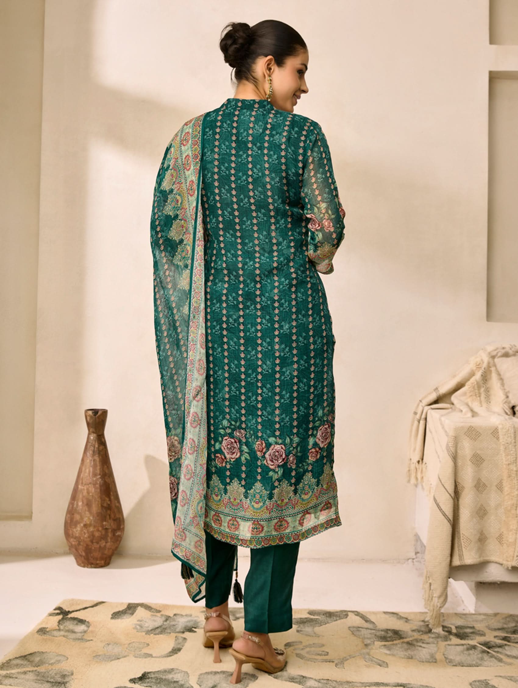 Woman wearing a green embroidered outfit in a room with decorative elements.