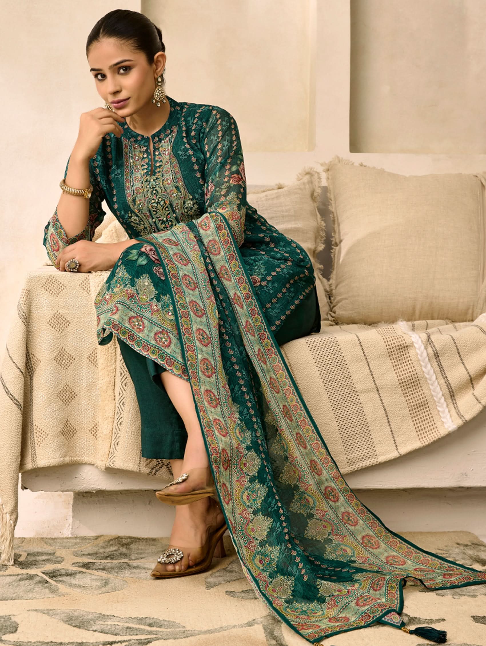 Woman in a green patterned dress sitting on a beige sofa in a living room.