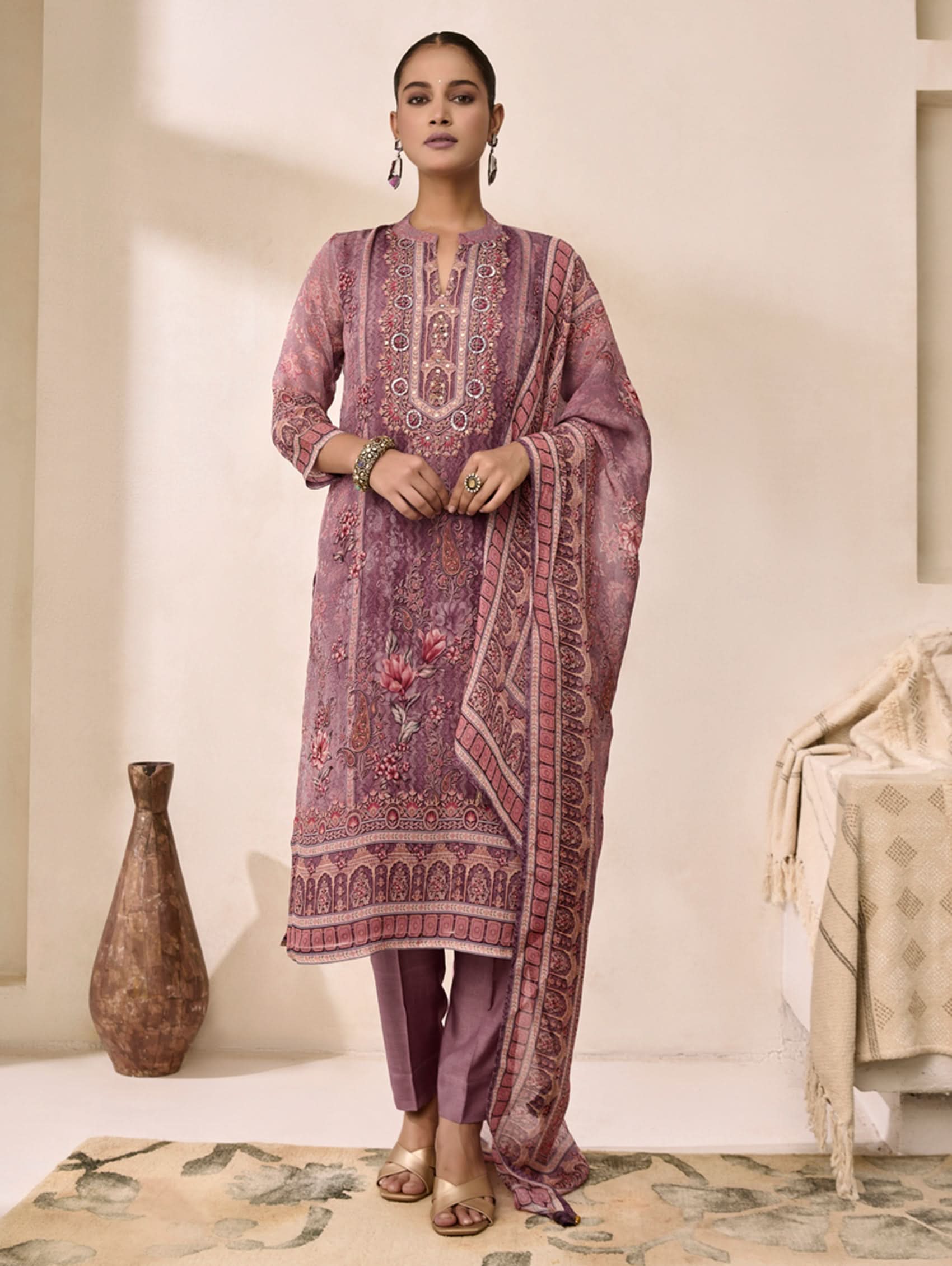 Woman wearing a traditional embroidered outfit in a decorated room.