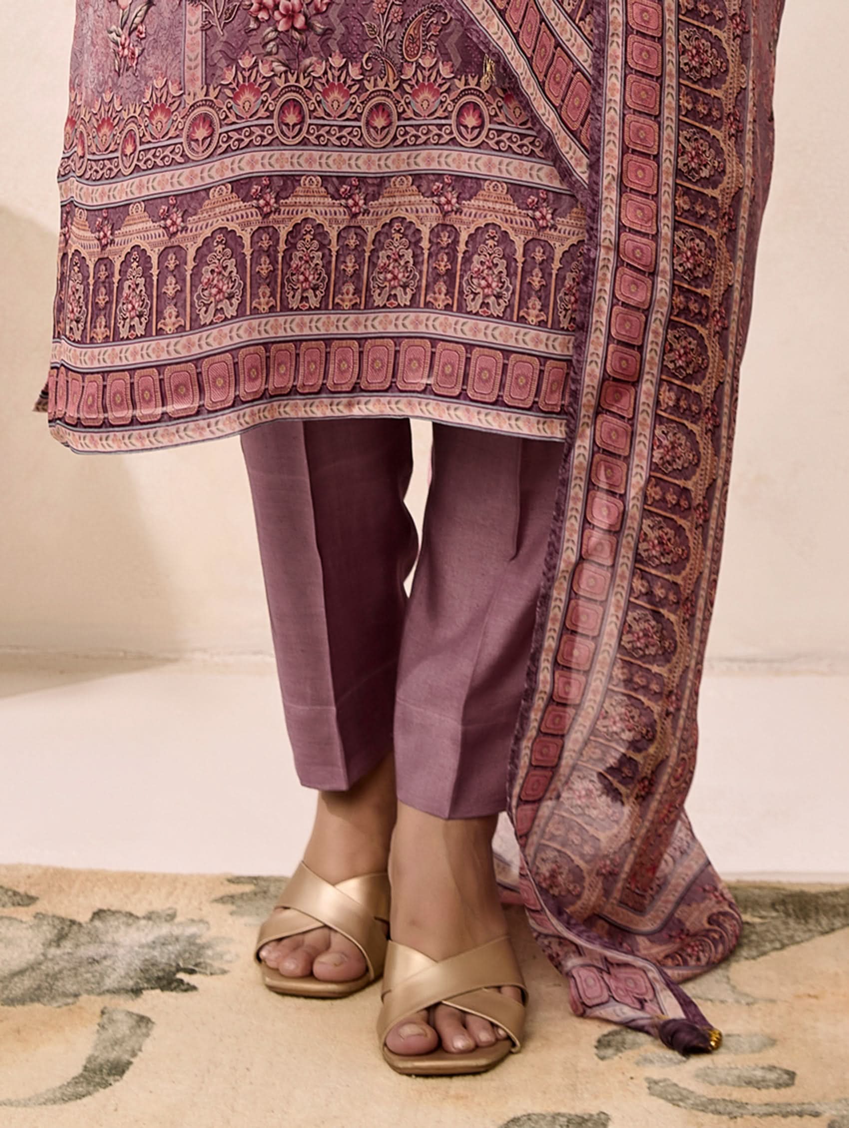 Person wearing a patterned dupatta over a plain outfit with gold sandals on a light background