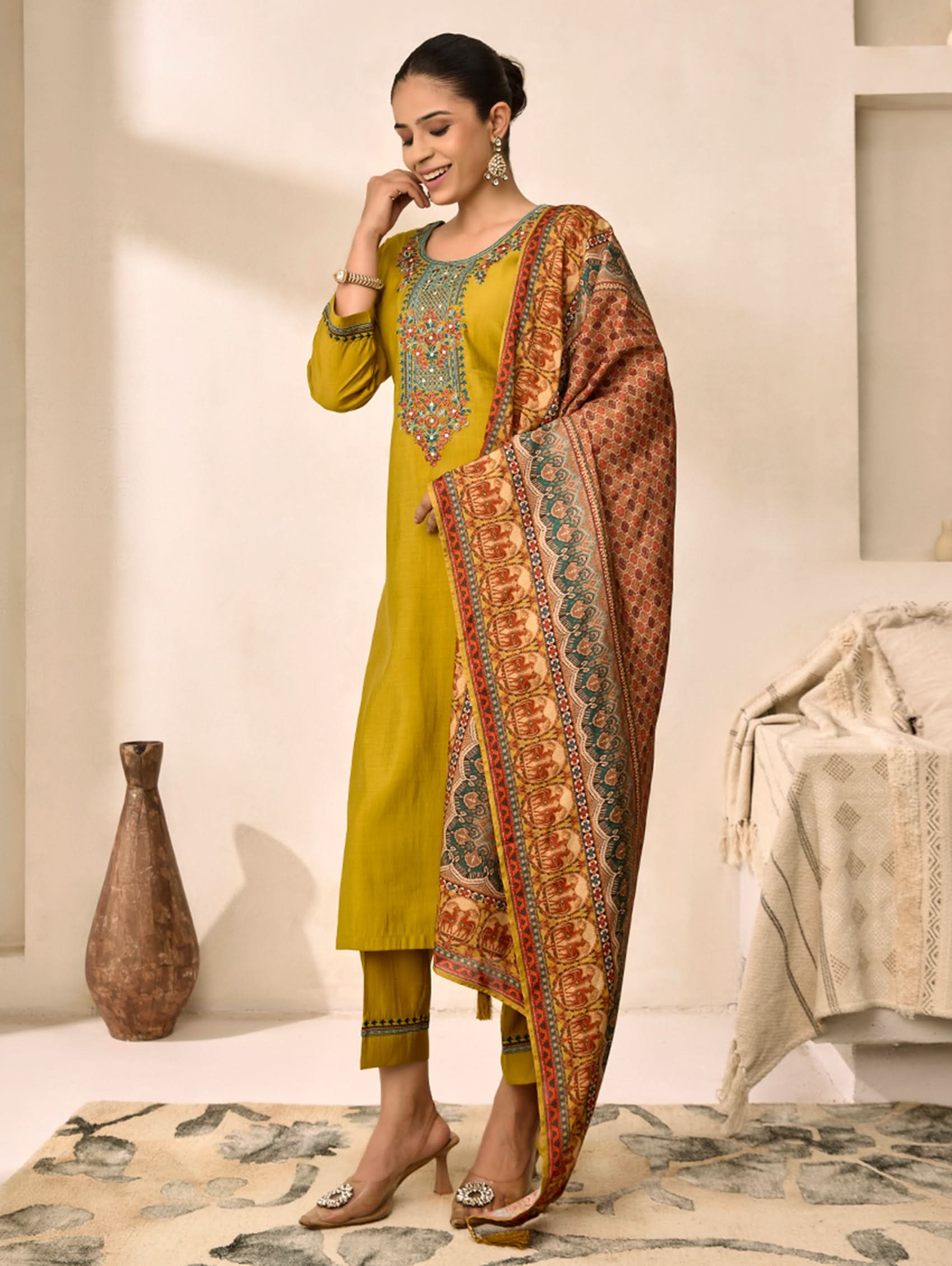 Woman wearing a yellow traditional outfit with a patterned dupatta in a minimalistic setting.