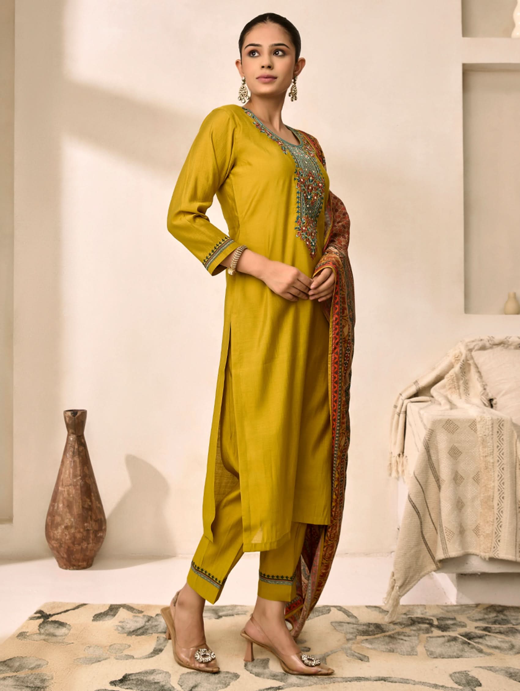 Woman wearing a mustard yellow traditional outfit with a patterned dupatta in a minimalistic room.