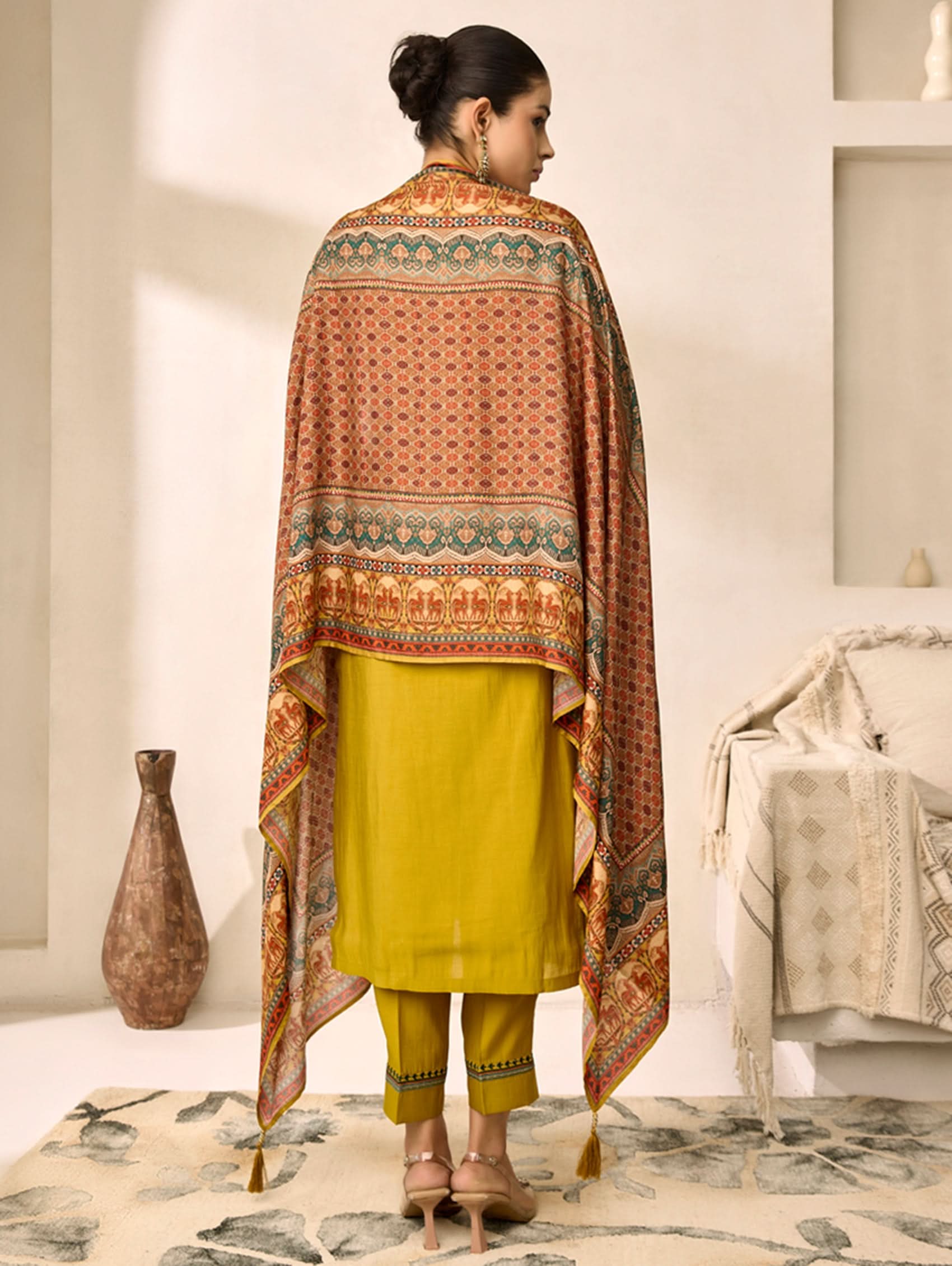 Woman wearing a yellow outfit with a patterned shawl in a minimalistic room.